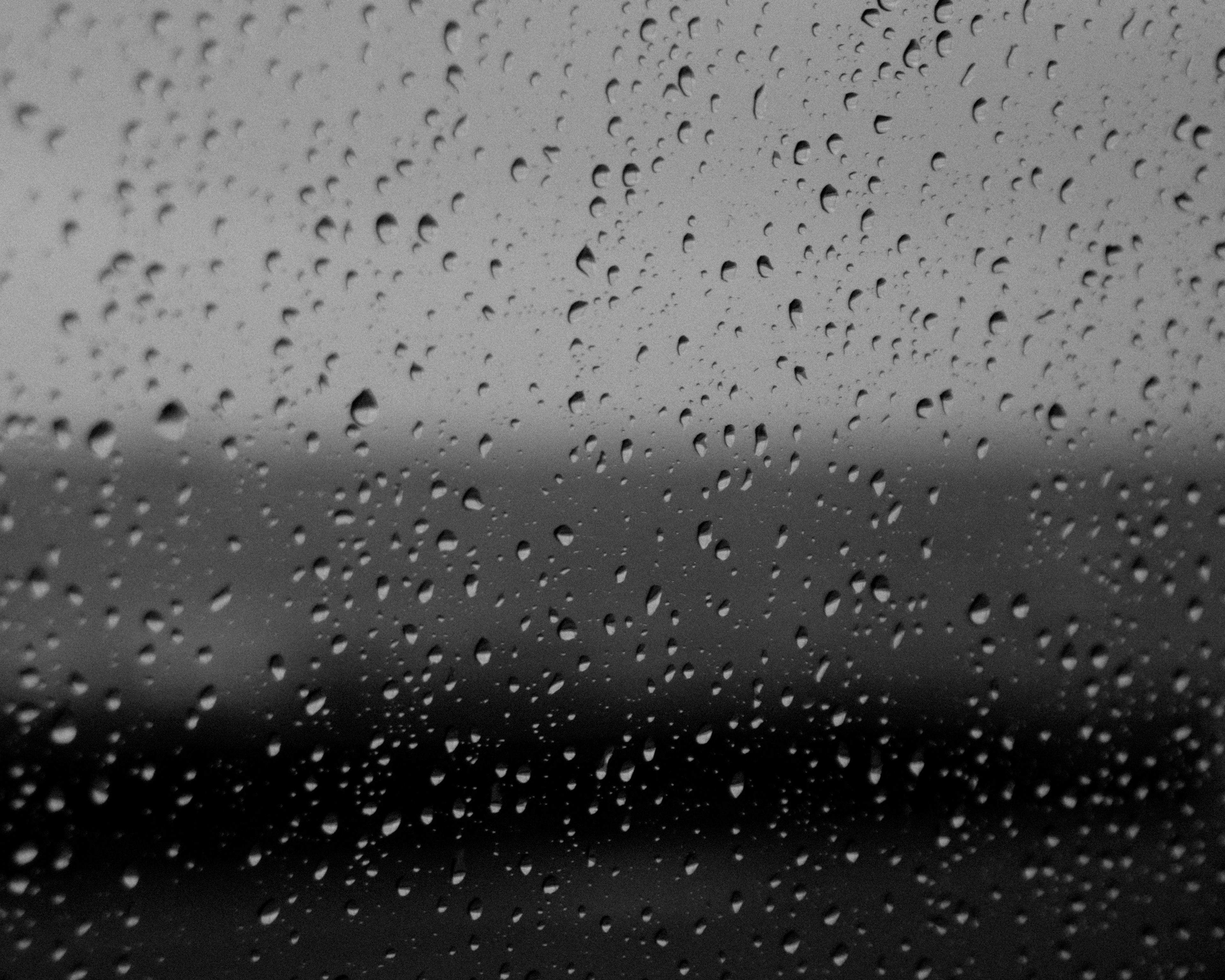 Foto en blanco y negro de gotas de lluvia en una ventana con un fondo borroso