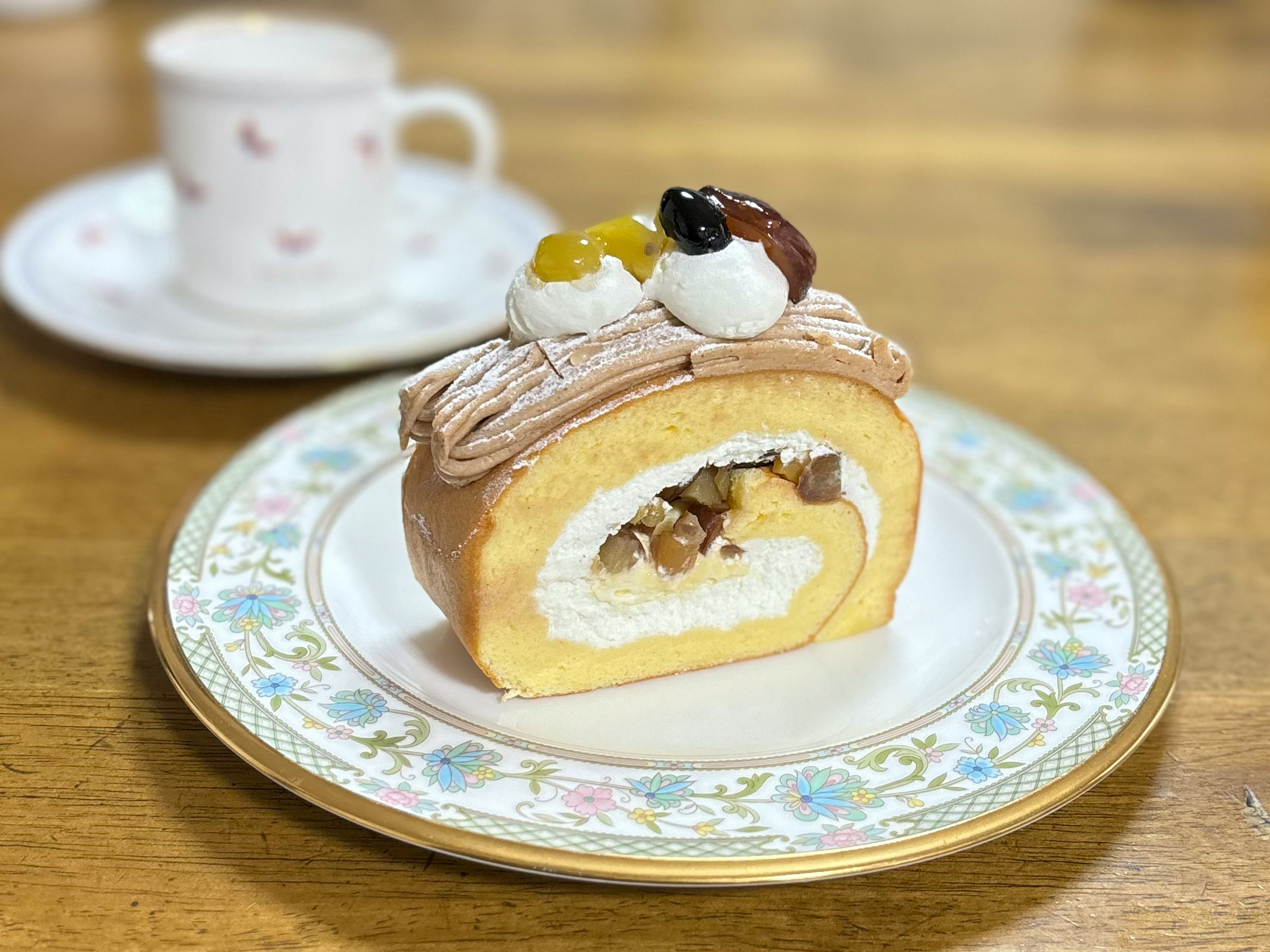 A beautifully presented roll cake topped with cream and nuts on an elegant plate