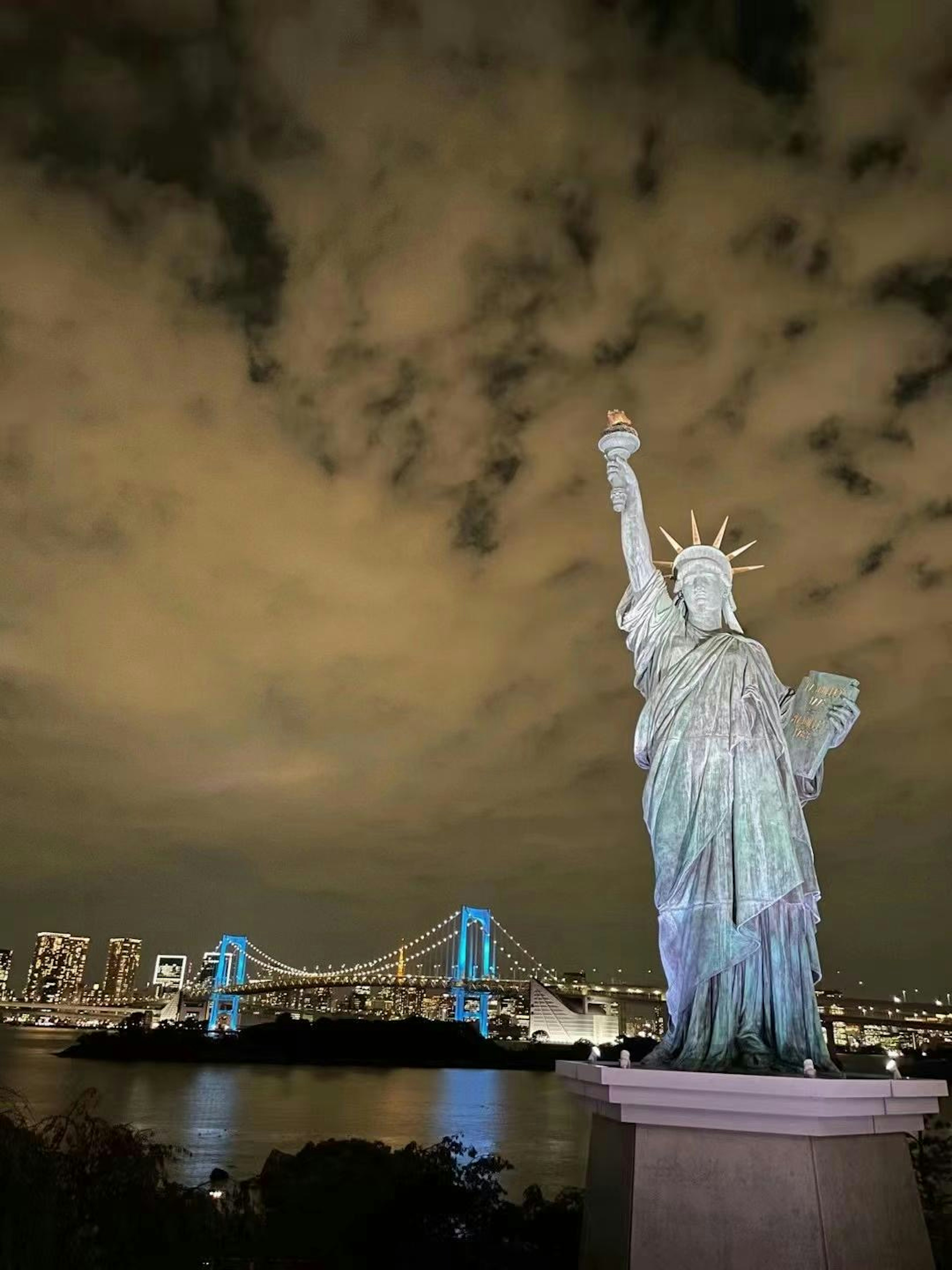 Estatua de la Libertad de noche con vista a la bahía de Tokio y el puente Rainbow al fondo