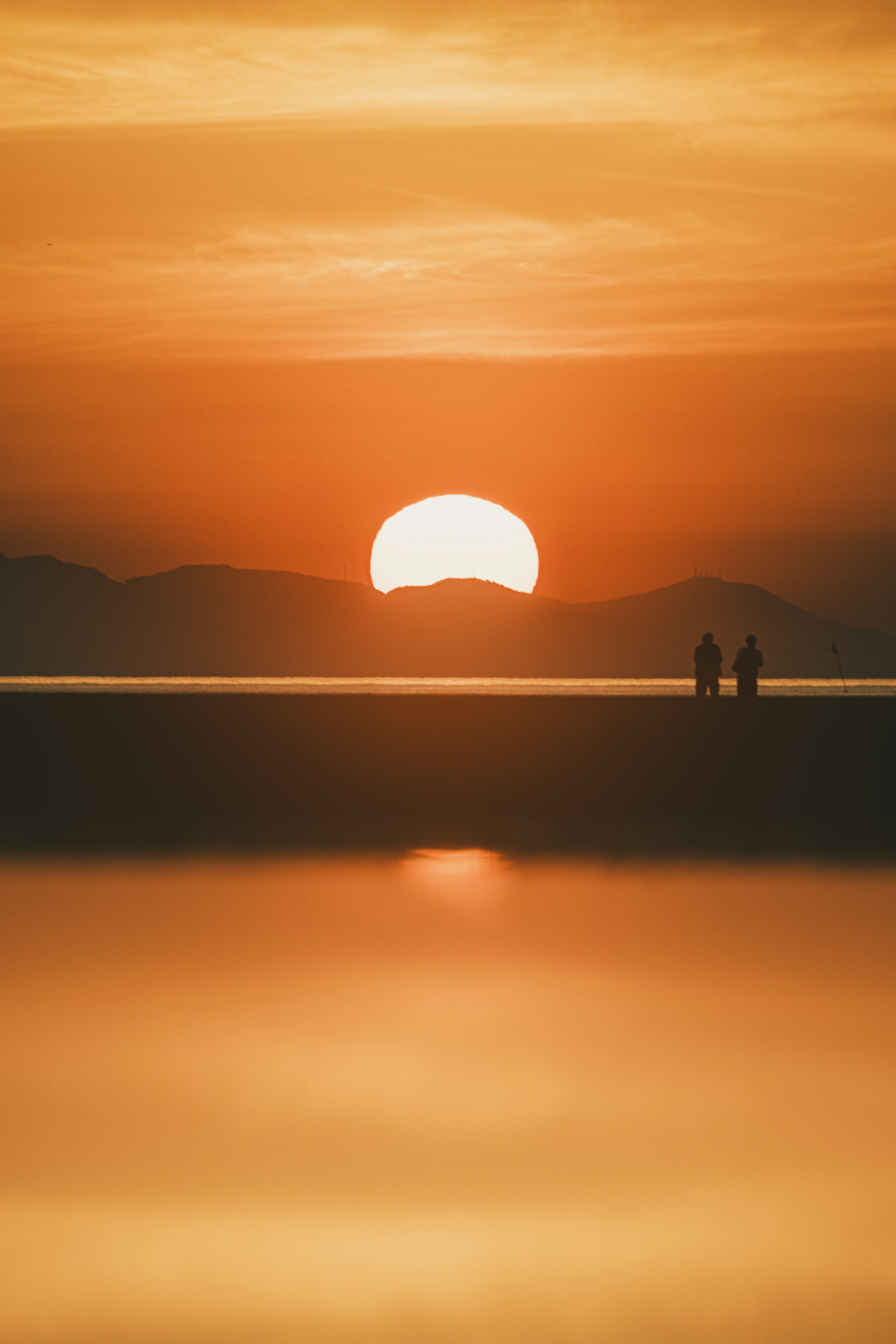 夕日が沈む海辺で二人の人が立っている風景