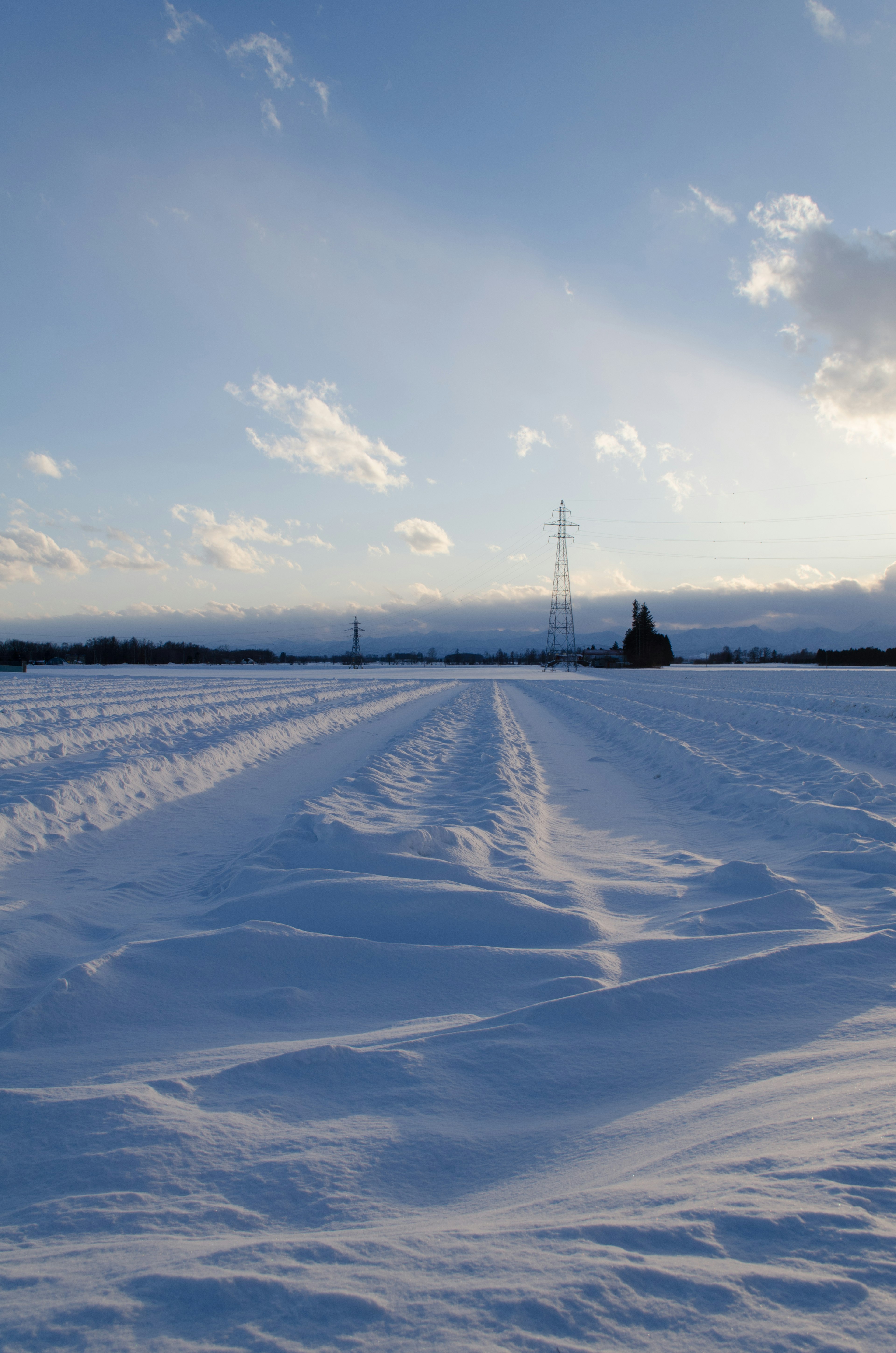 Verschneite Landschaft unter einem blauen Himmel mit entfernten Stromleitungen