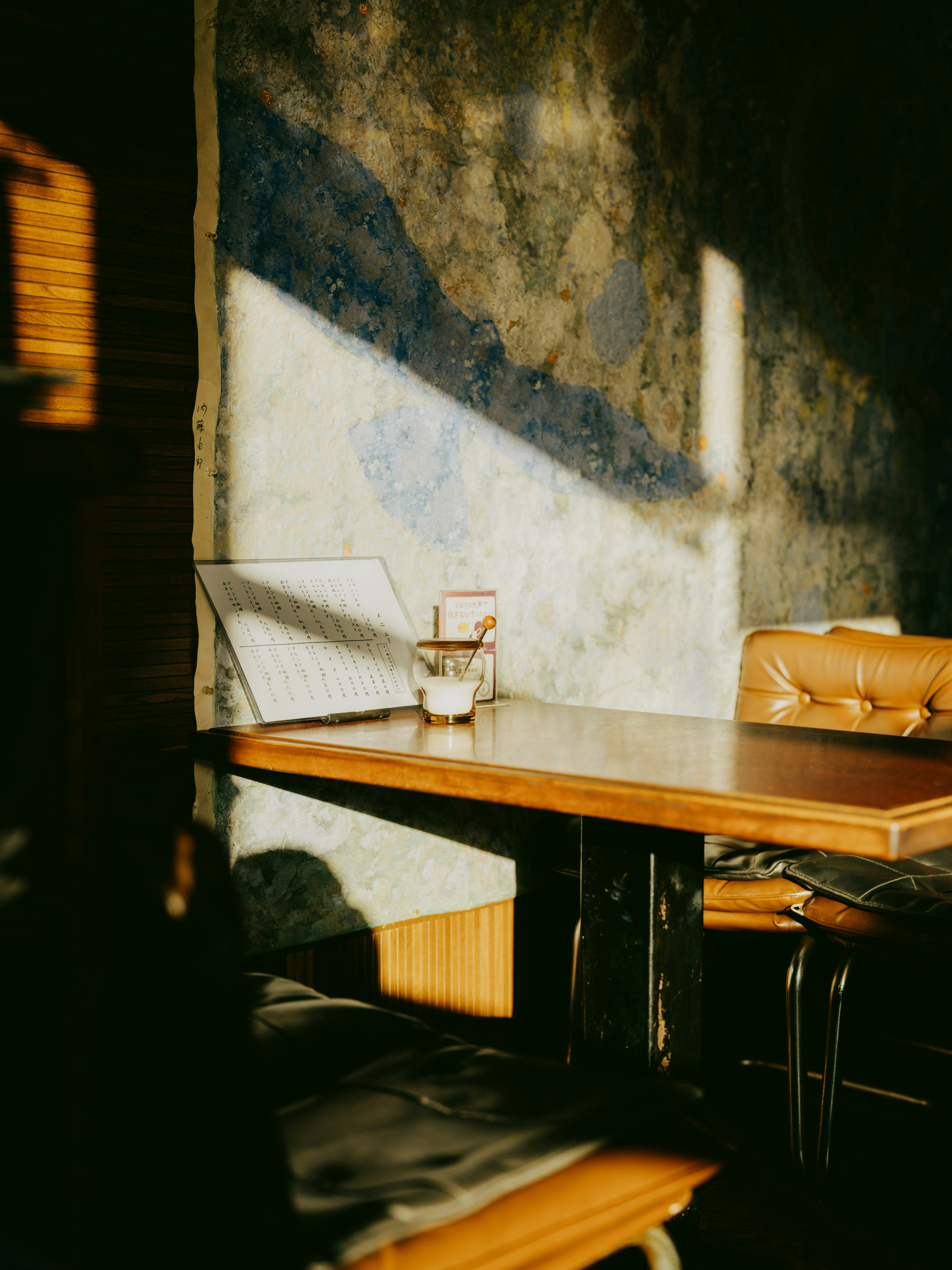 Angolo caffè accogliente con tavolo in legno e sedie in pelle luce solare che proietta ombre sul muro