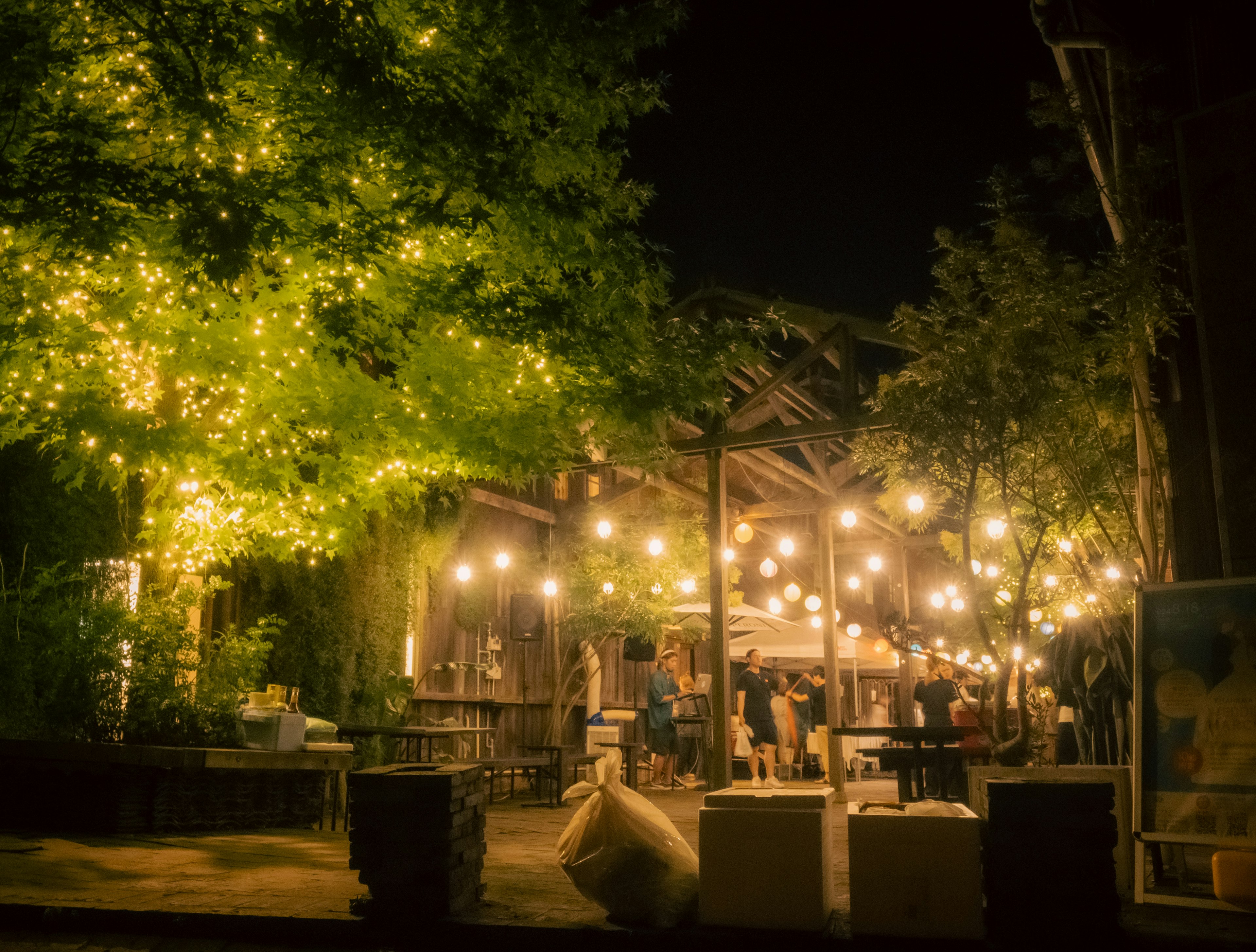 Outdoor dining area at night with glowing lights and green trees