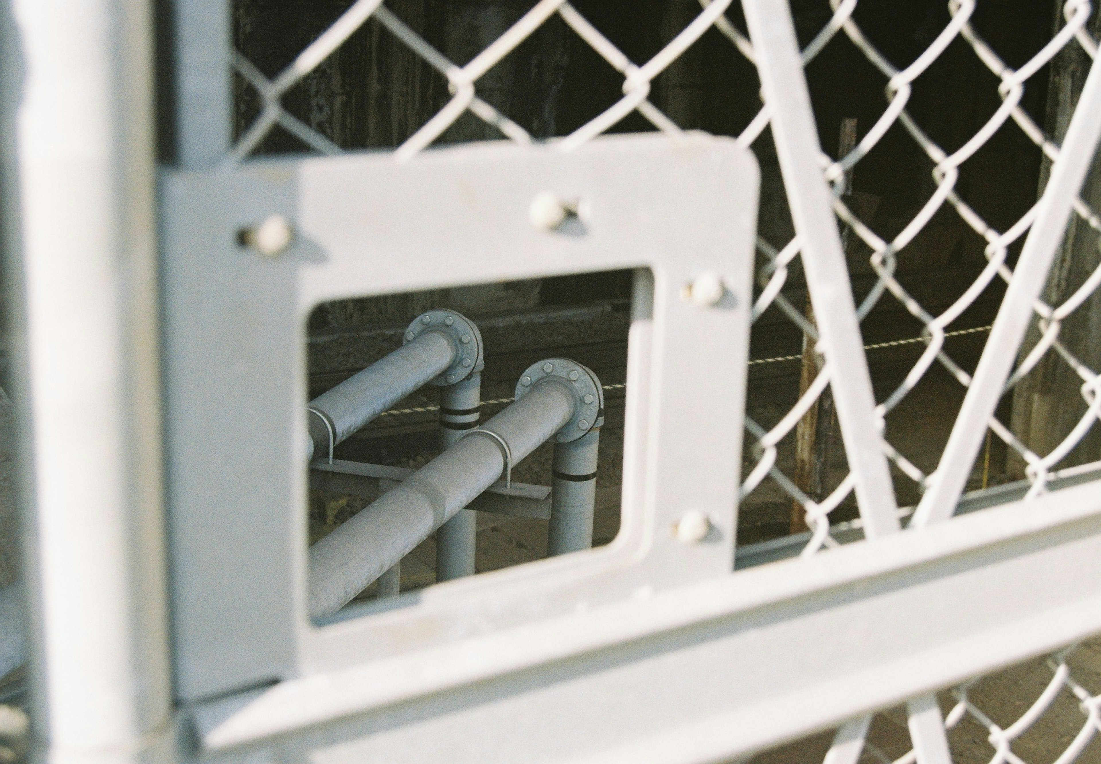 A view through a metal mesh fence showing pipes inside a square opening