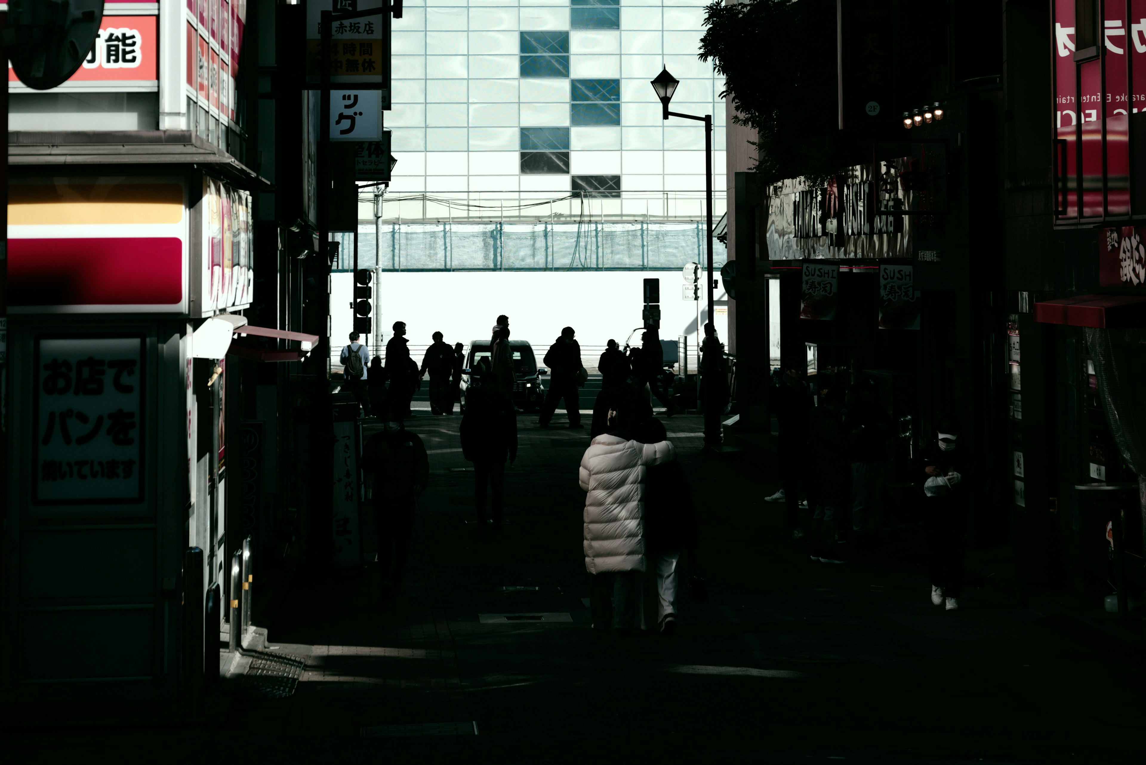 Silhouettes of people walking through a city street with buildings in the background