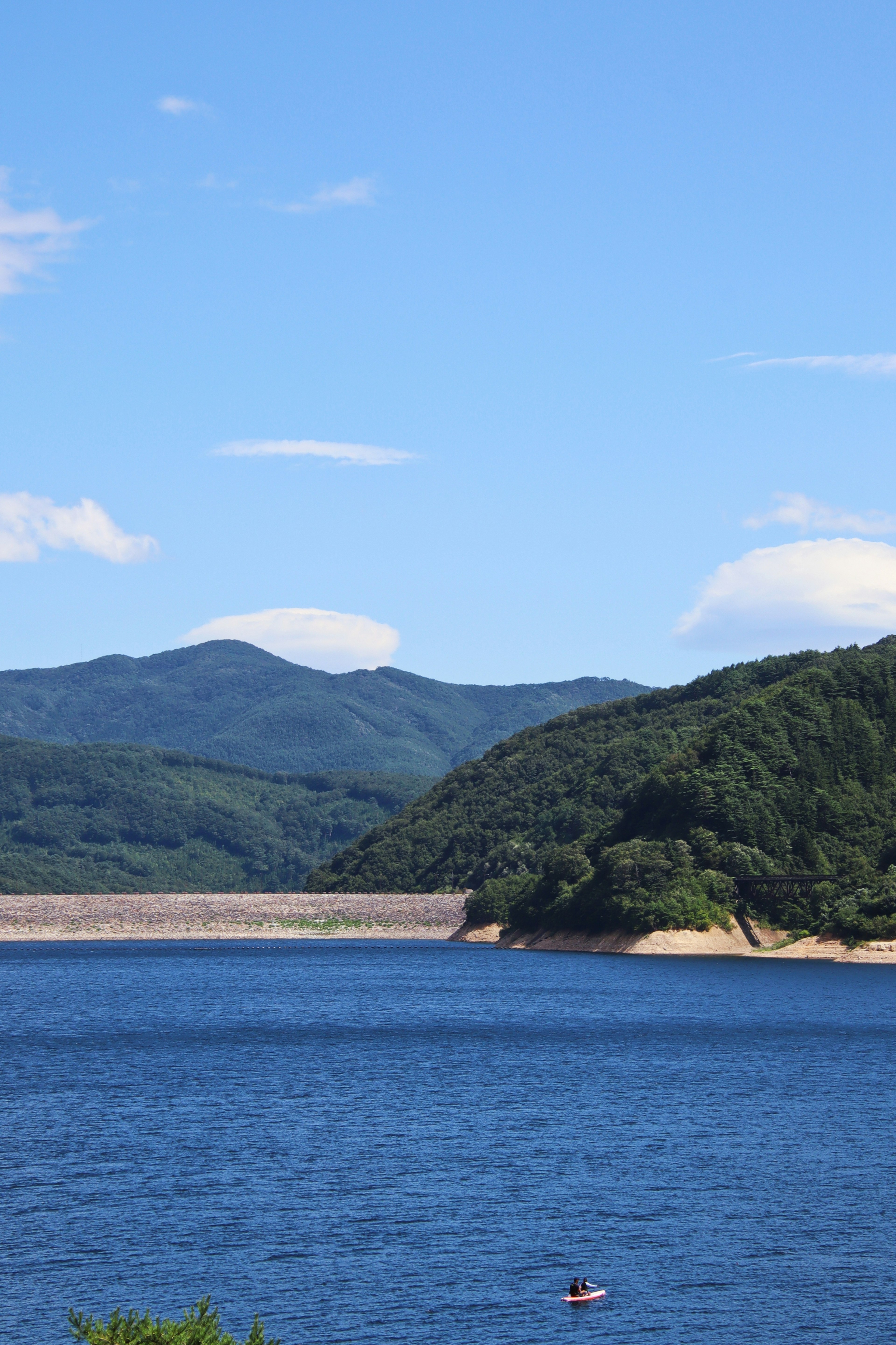 Vista escénica de un lago tranquilo con cielo azul y montañas verdes al fondo