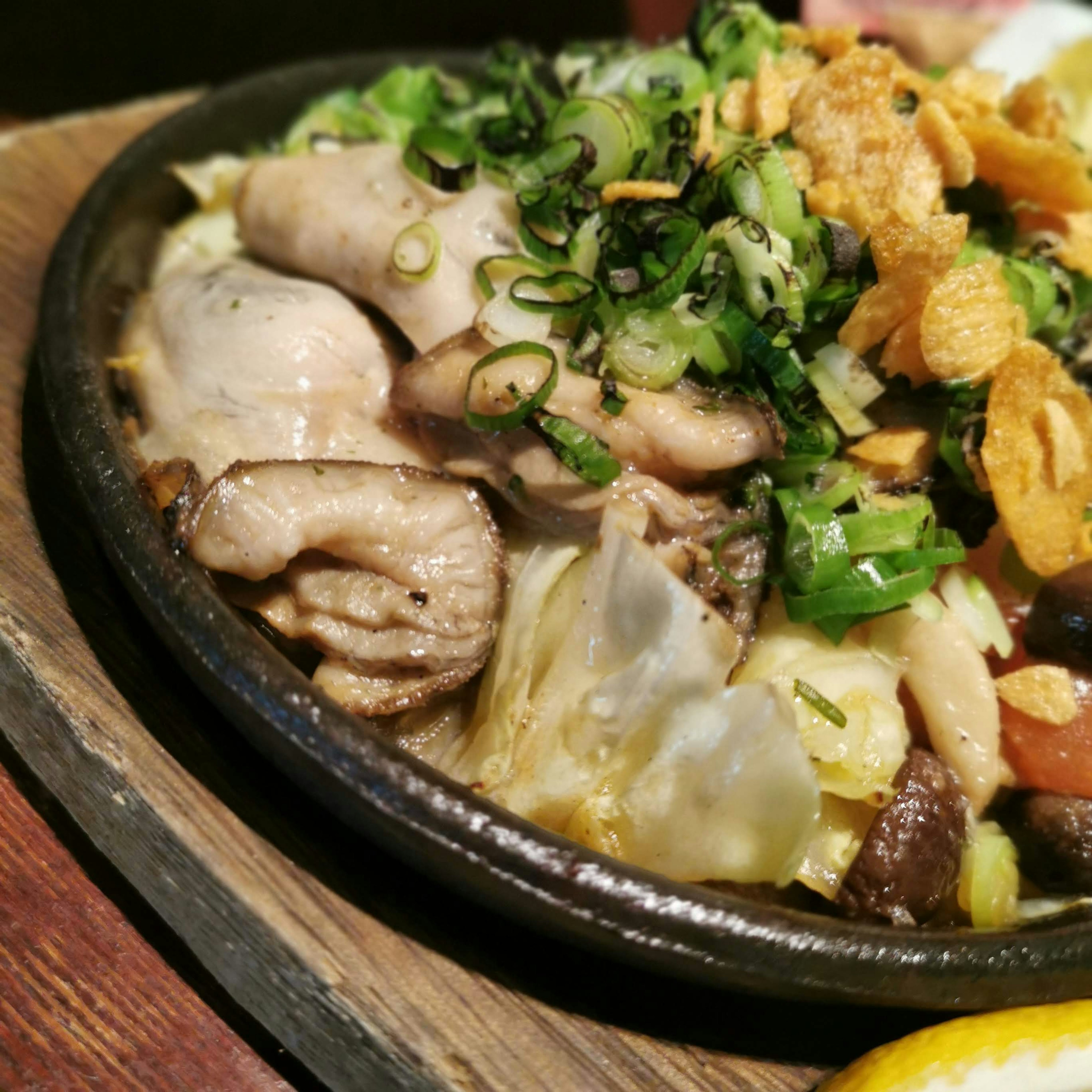 Sizzling dish on a hot plate featuring chicken and vegetables topped with green onions and crispy garlic