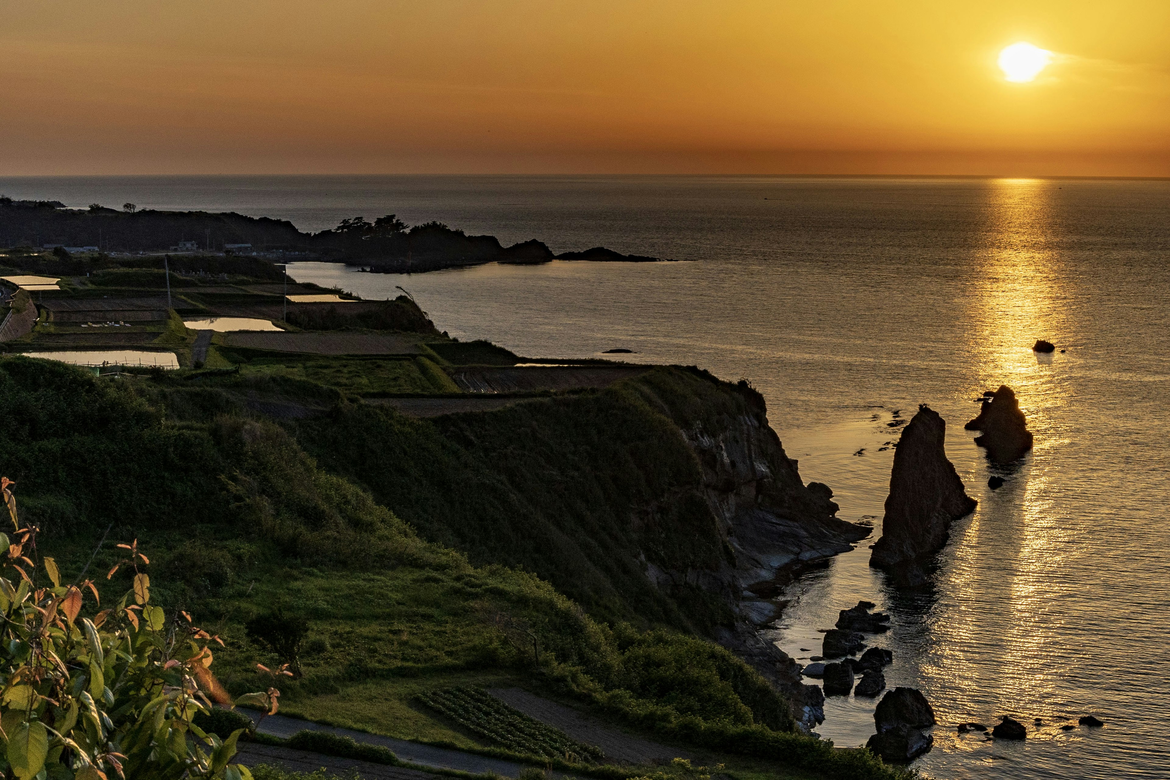 Vista escénica de un atardecer sobre el mar con acantilados verdes y formaciones rocosas