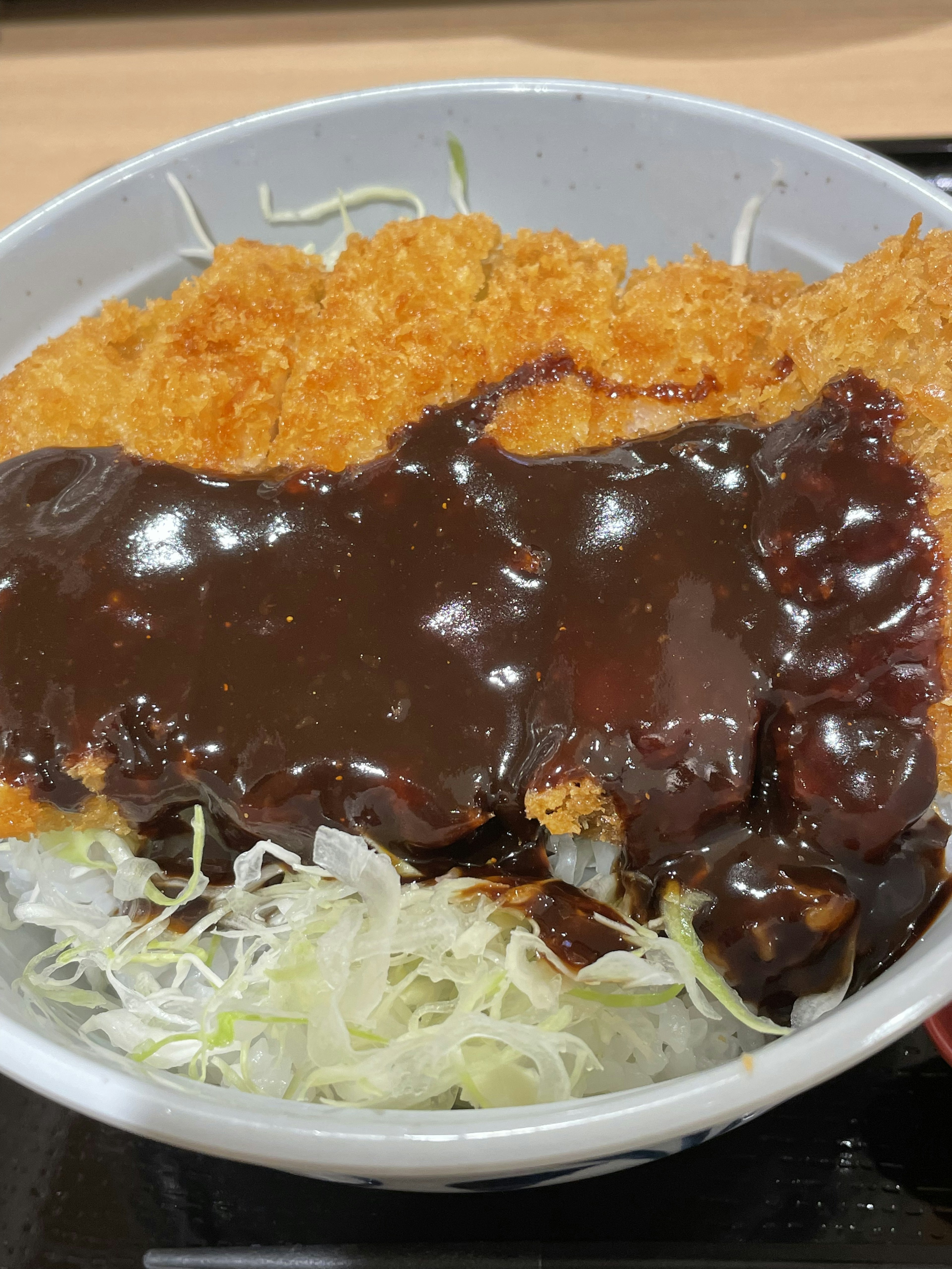 Eine Schüssel Katsu Don mit knusprigem paniertem Schnitzel, garniert mit dunkler Sauce und gehobeltem Kohl