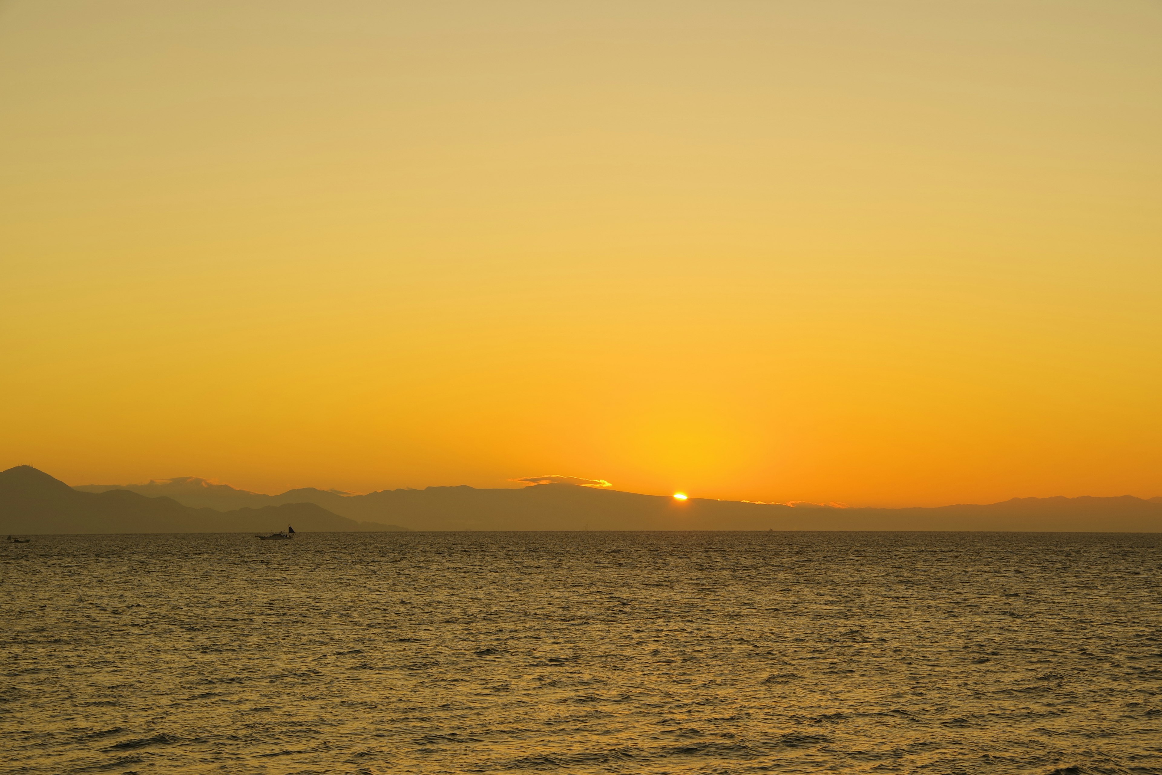 Meereslandschaft bei Sonnenuntergang mit orangefarbenem Himmel und Bergsilhouetten