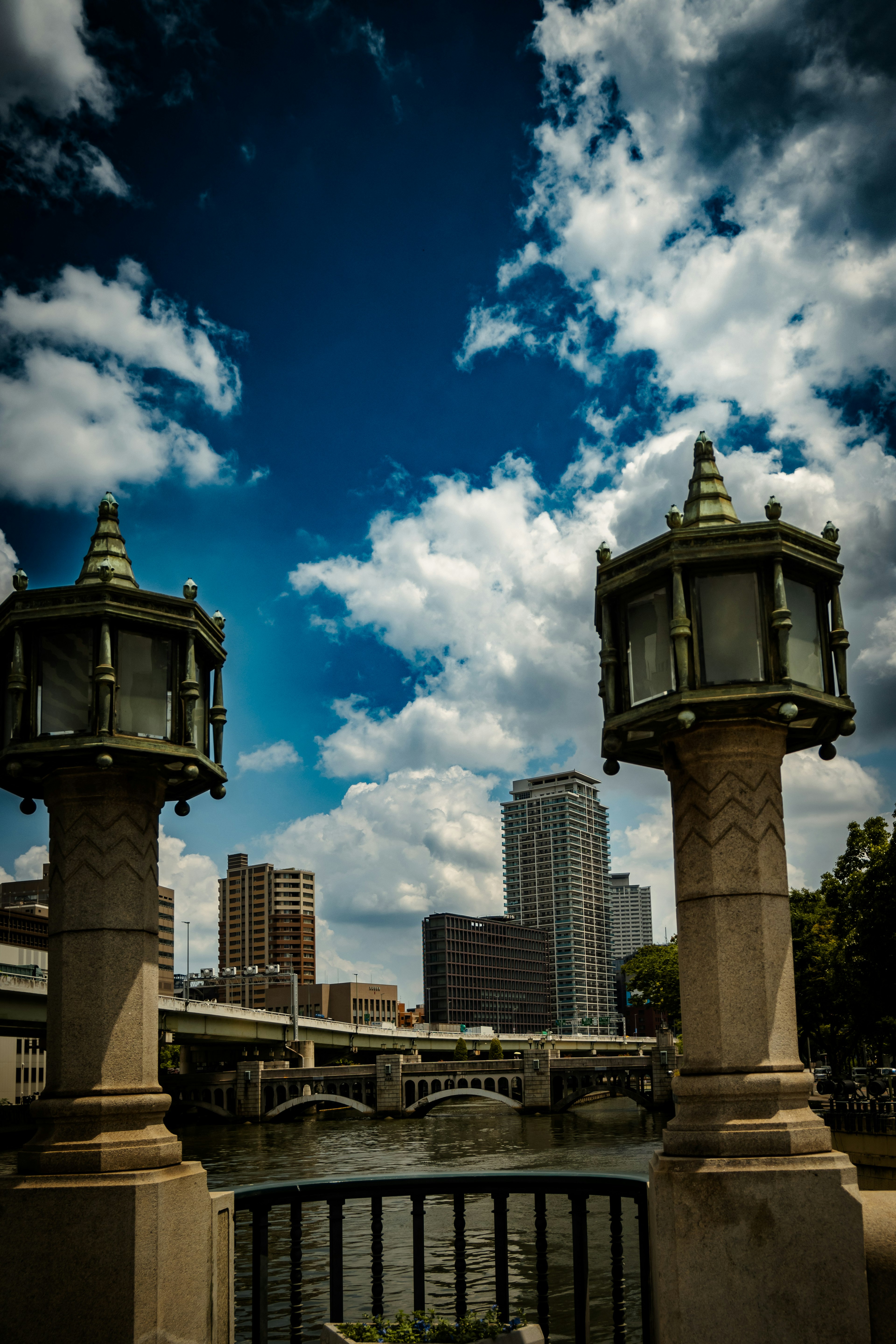 Dos farolas ornamentadas enmarcando una vista del río con un horizonte urbano bajo un cielo azul