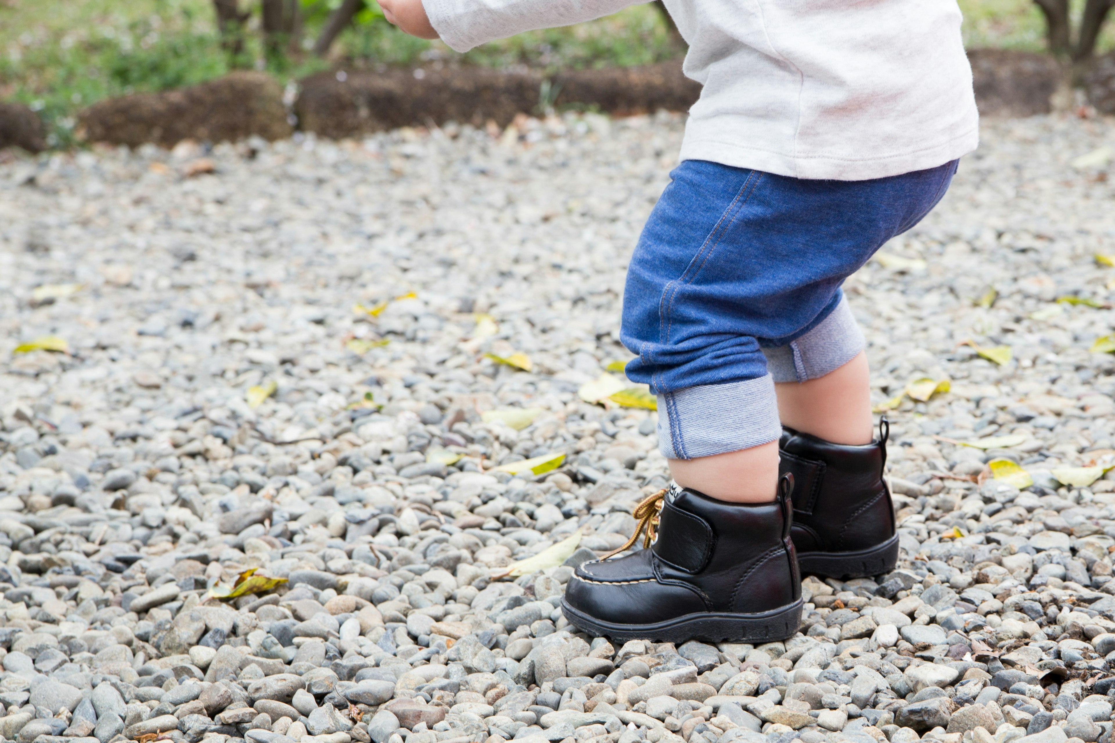 Anak berjalan di atas kerikil mengenakan sepatu bot hitam dan celana jeans digulung