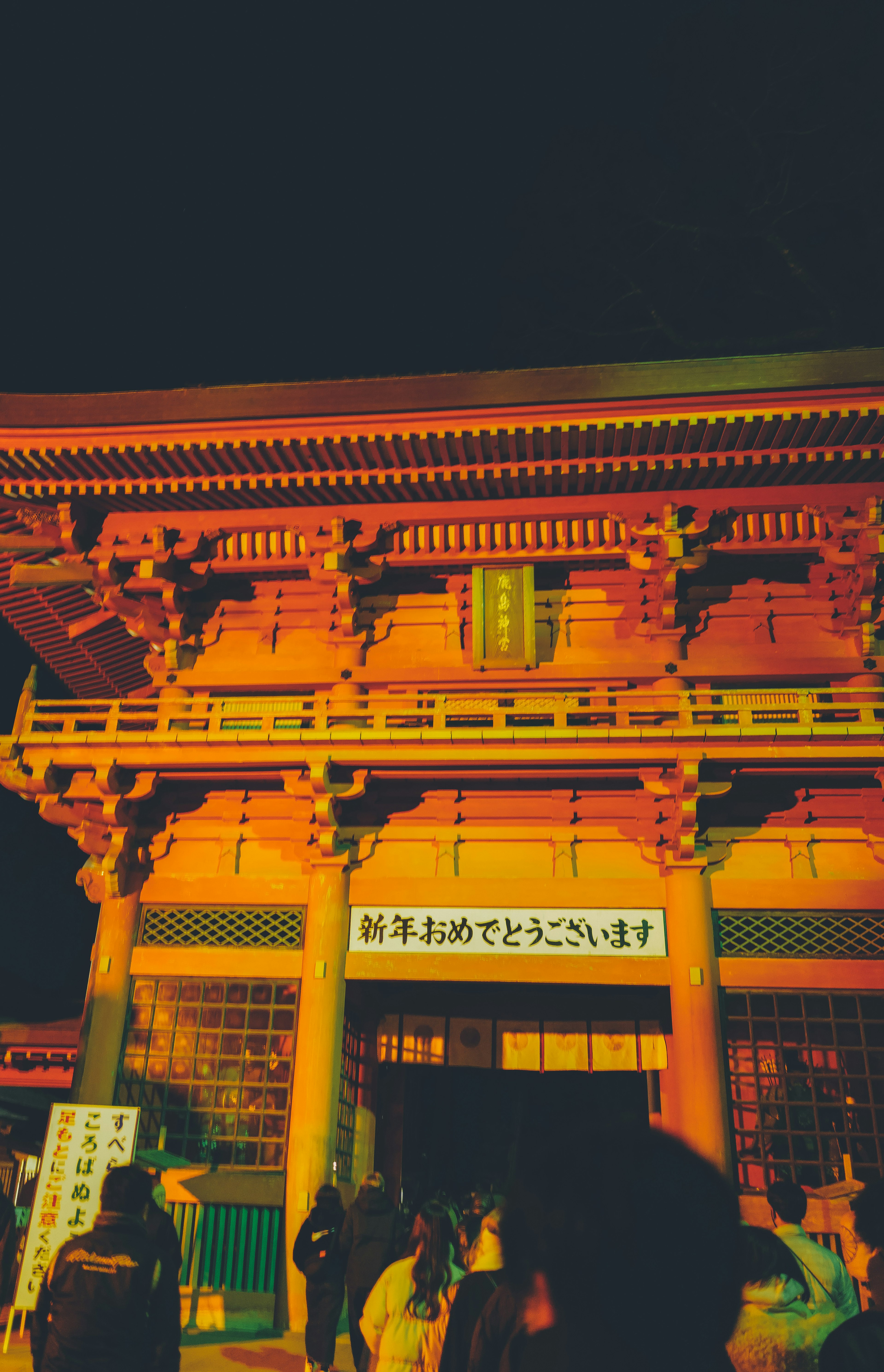 Una puerta de templo japonés tradicional iluminada por la noche con personas reunidas