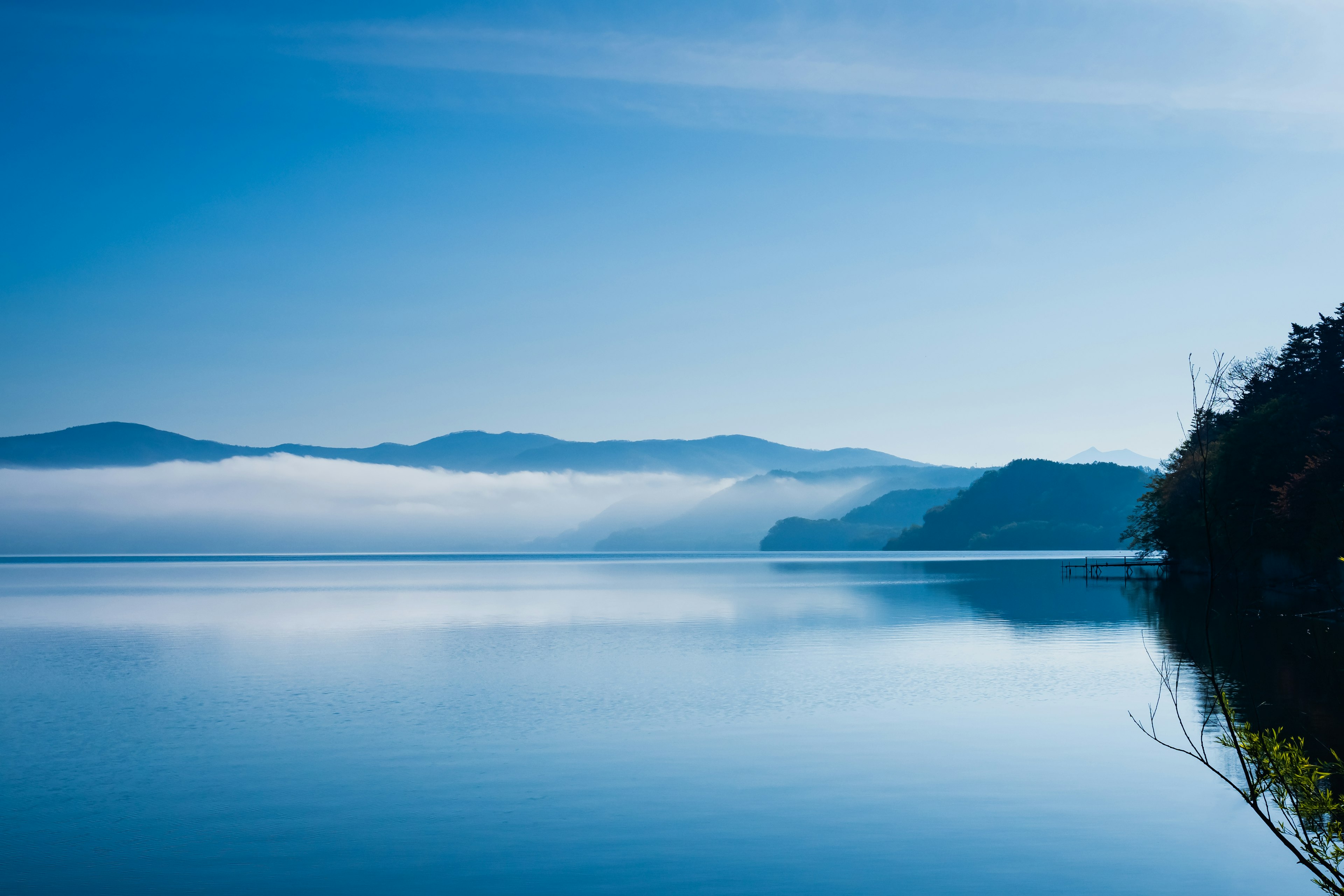 Szenische Aussicht auf einen blauen See, umgeben von nebligen Bergen