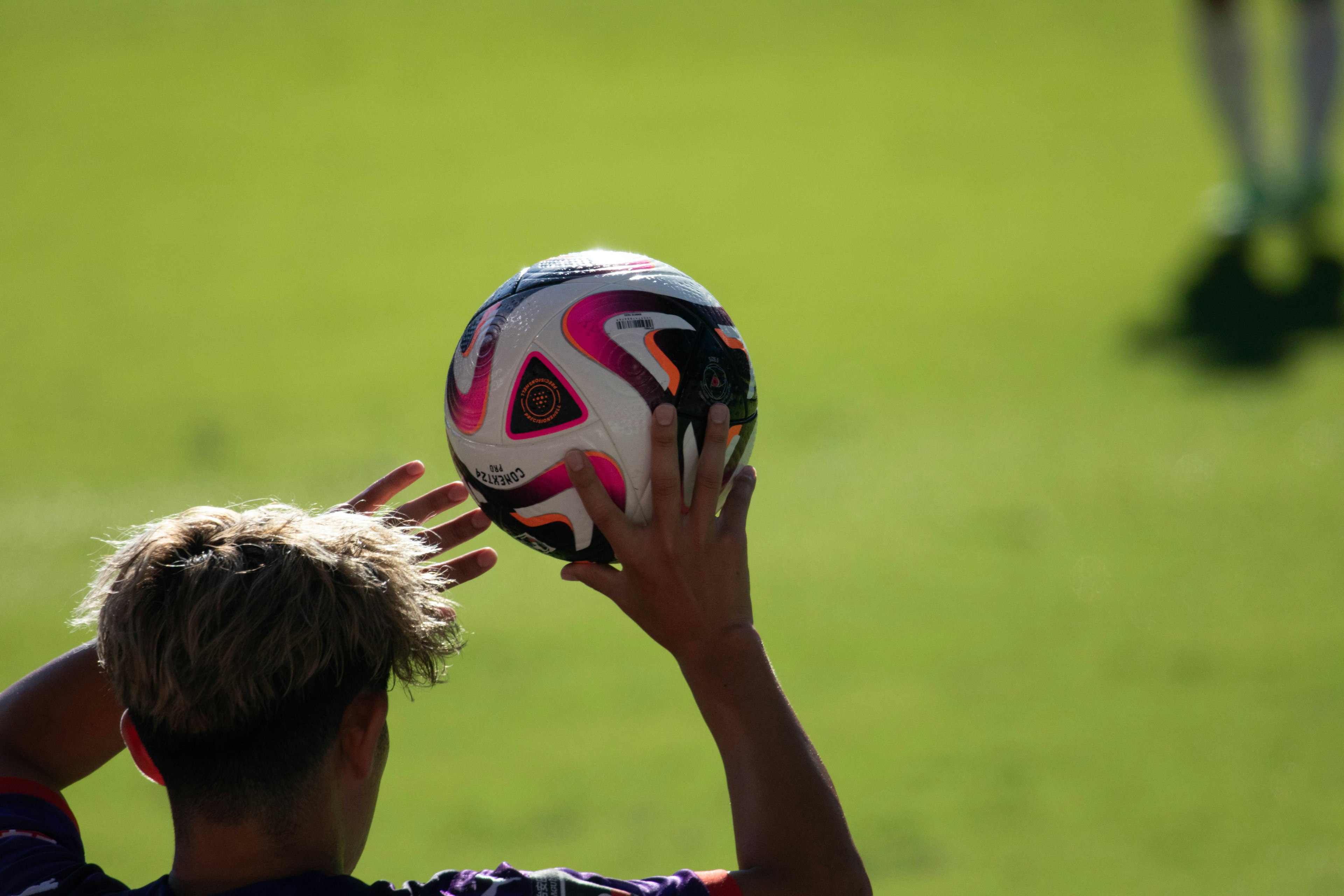 Jugador sosteniendo un balón de fútbol con fondo de césped verde