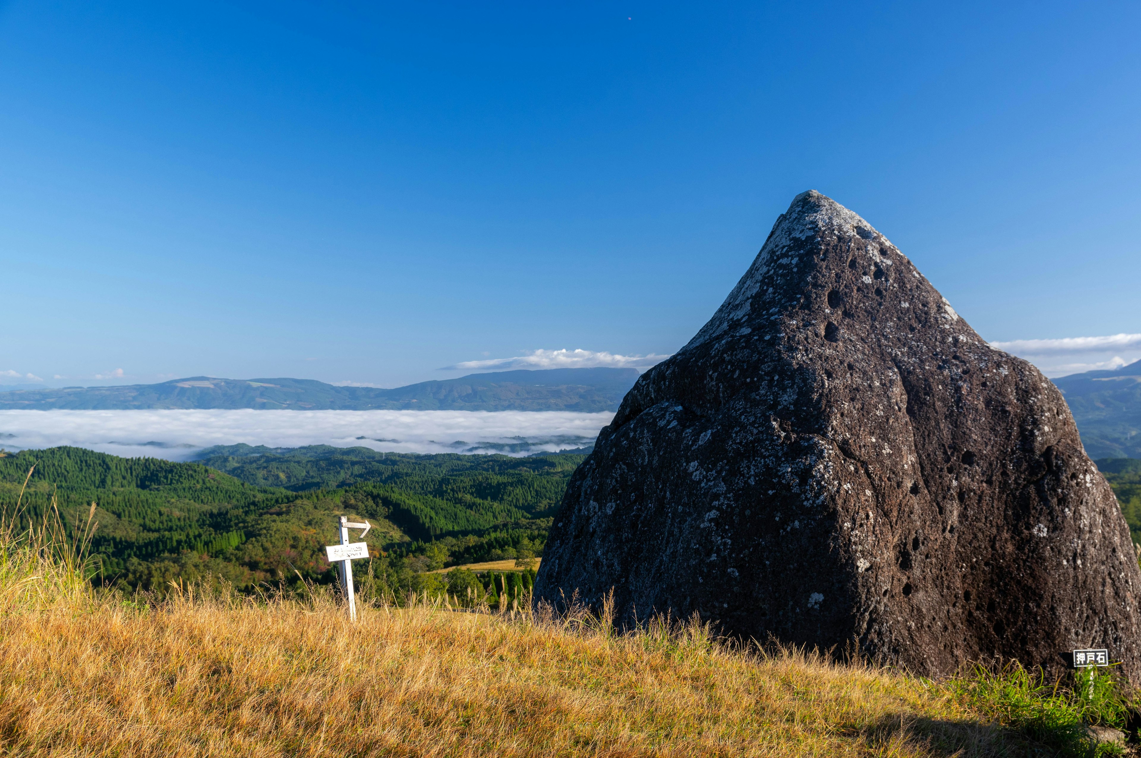 Large rock under blue sky with green hills in the background