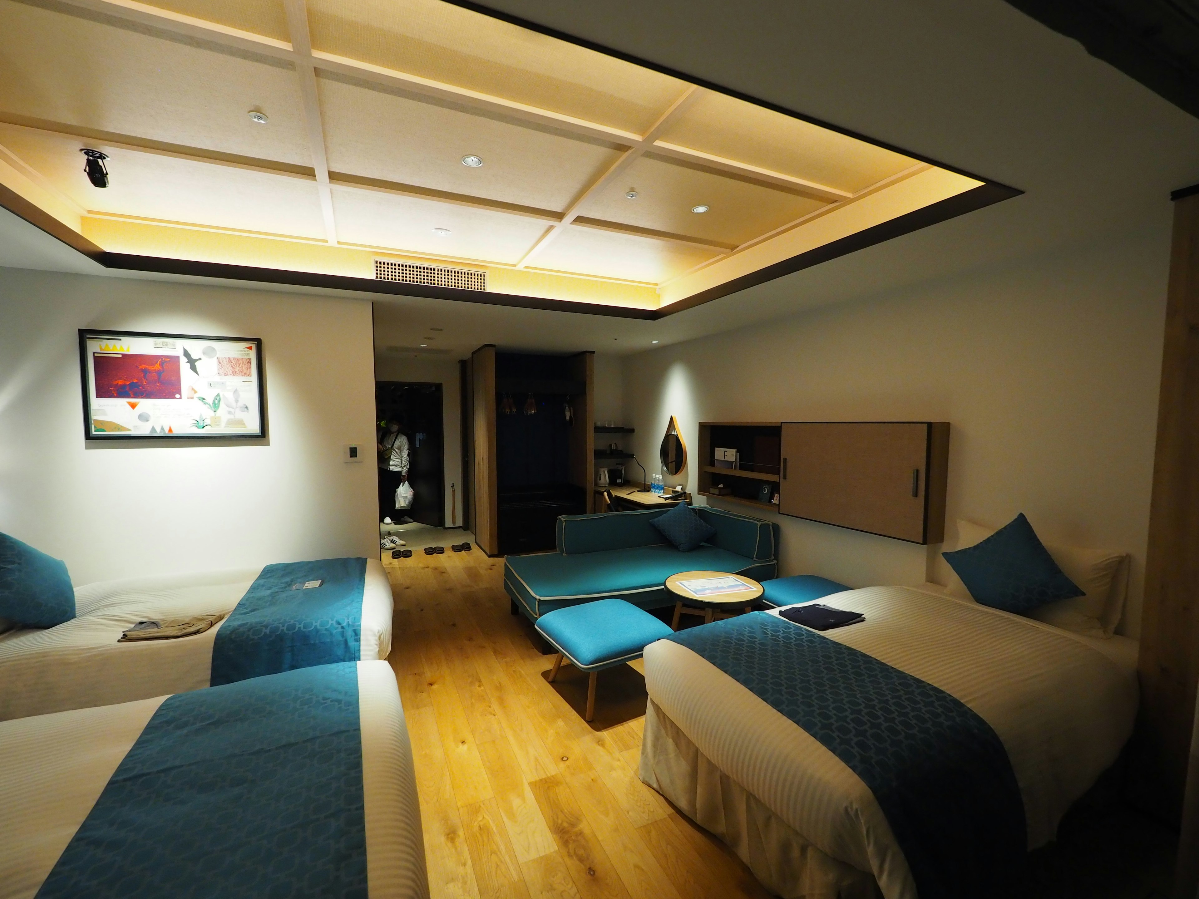 Modern hotel room featuring two beds and a living area with blue cushions wooden floor and ambient lighting