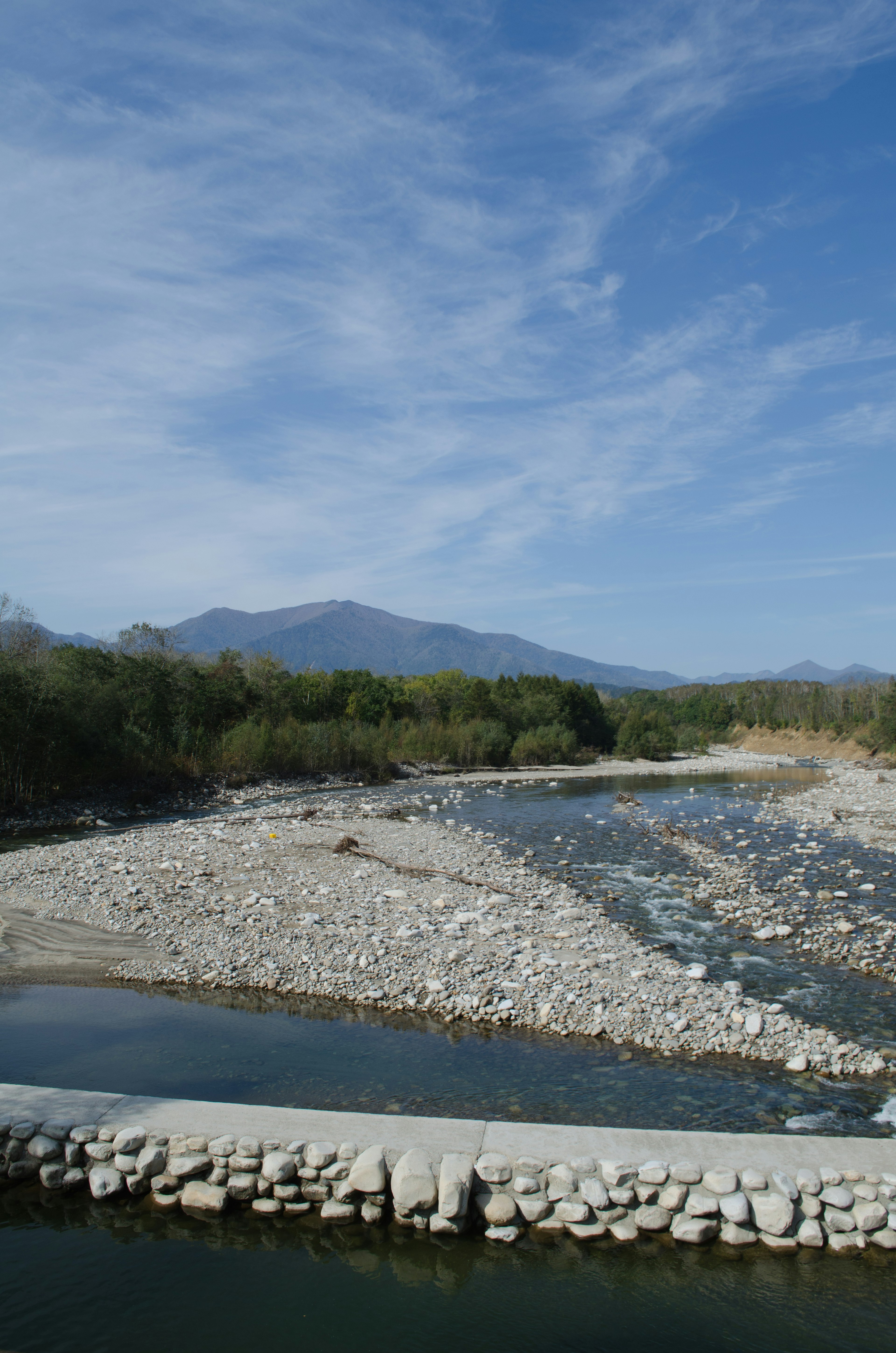 青空の下に流れる川と石の堤防が見える風景