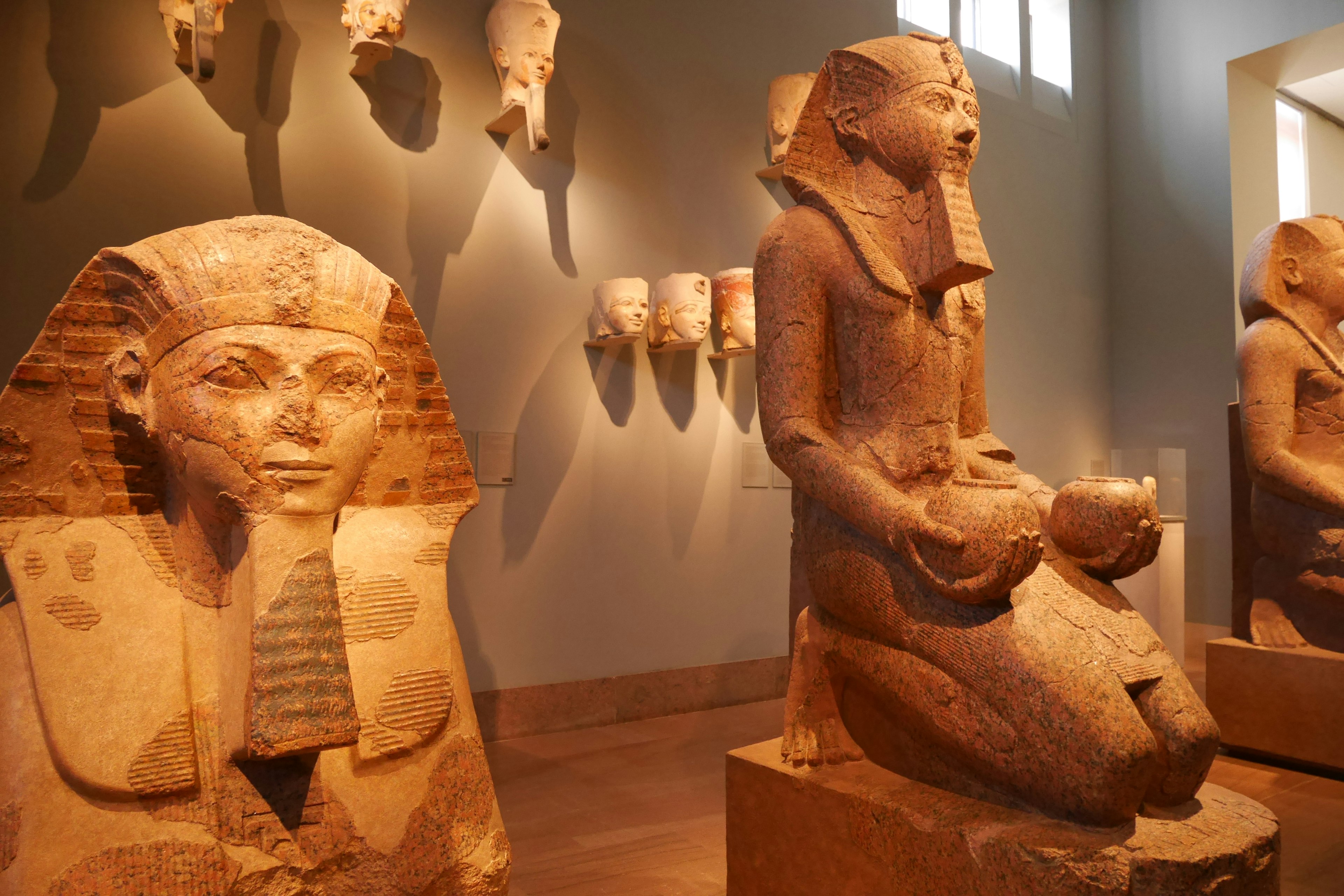 Egyptian sculptures displayed in a museum featuring a sphinx and a goddess statue