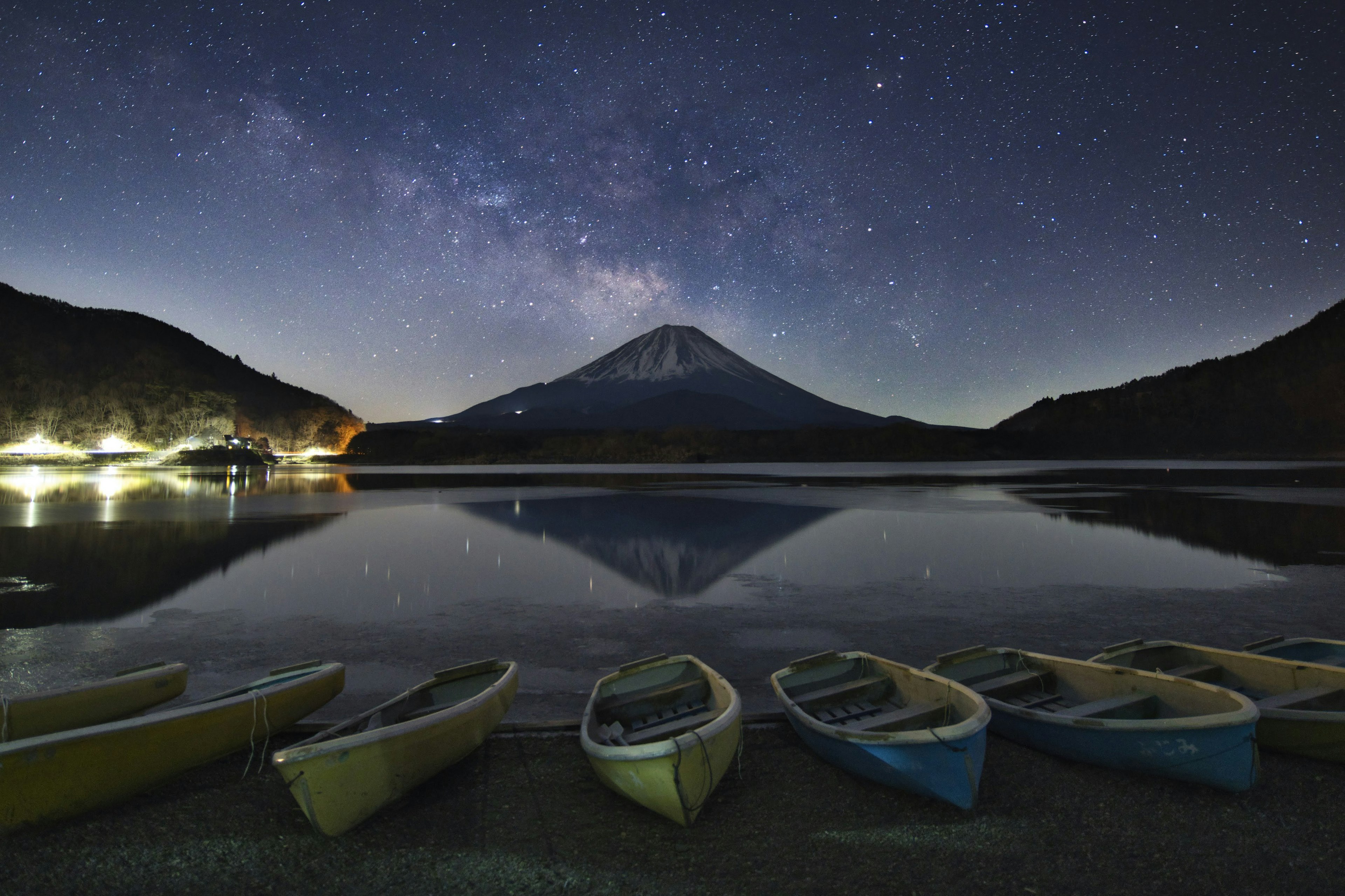 富士山在星空下映照在湖面的景色，旁邊排成一列的獨木舟