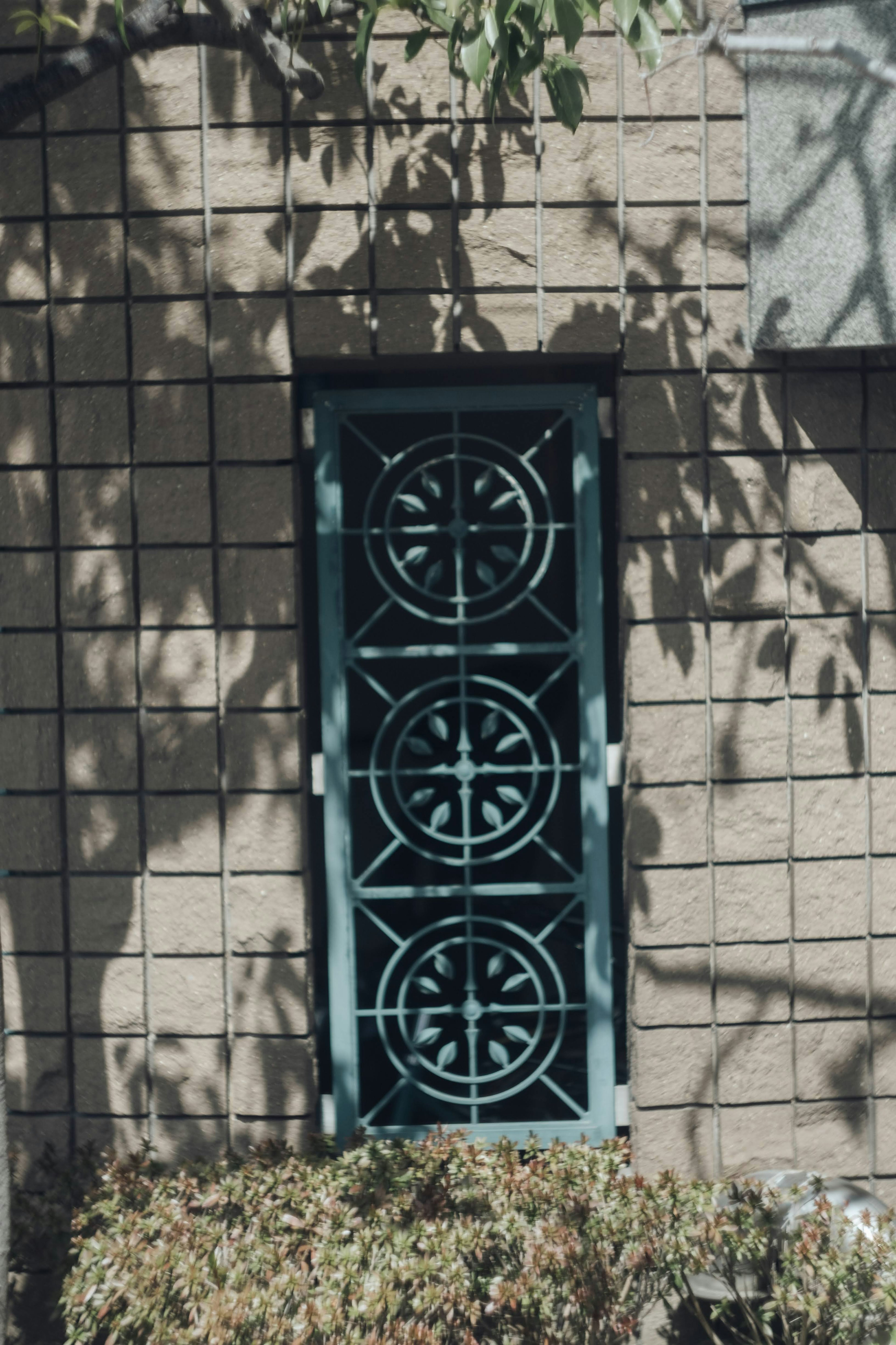 Grille de fenêtre verte décorative avec des motifs circulaires contre un mur en briques