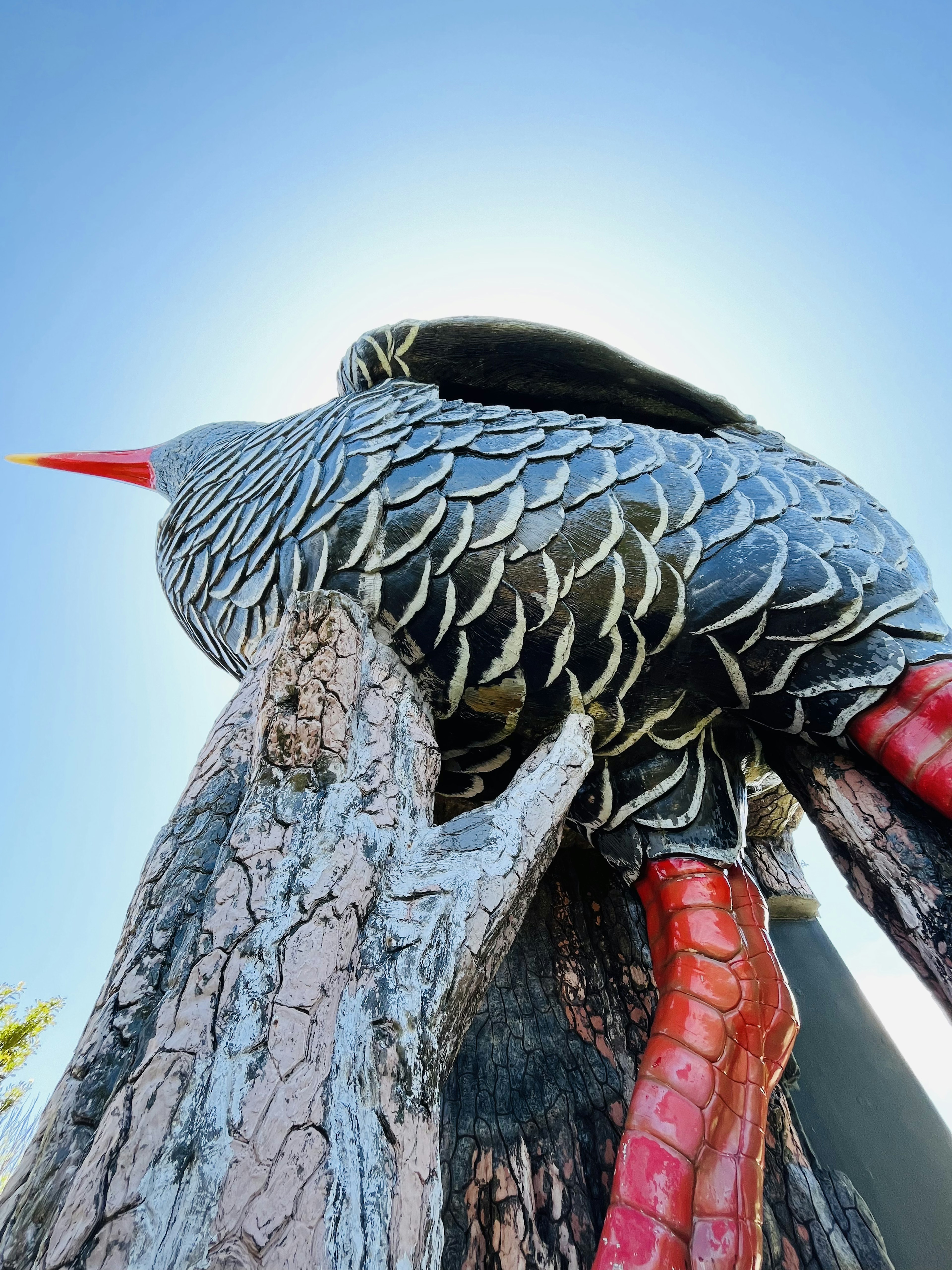 Grande sculpture d'oiseau perchée sur un tronc d'arbre avec un bec rouge proéminent et des plumes détaillées