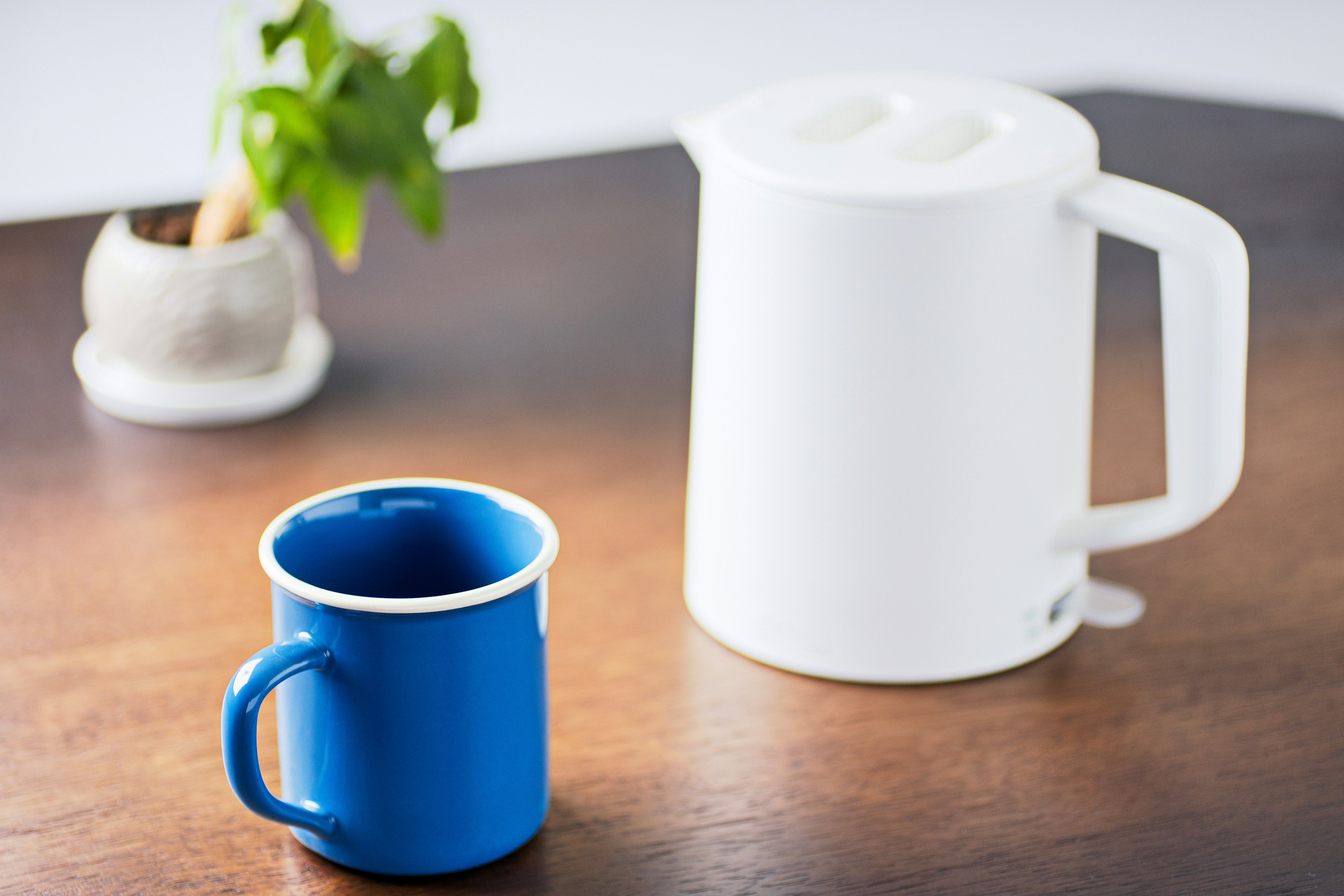 Una taza azul y una tetera blanca sobre una mesa de madera