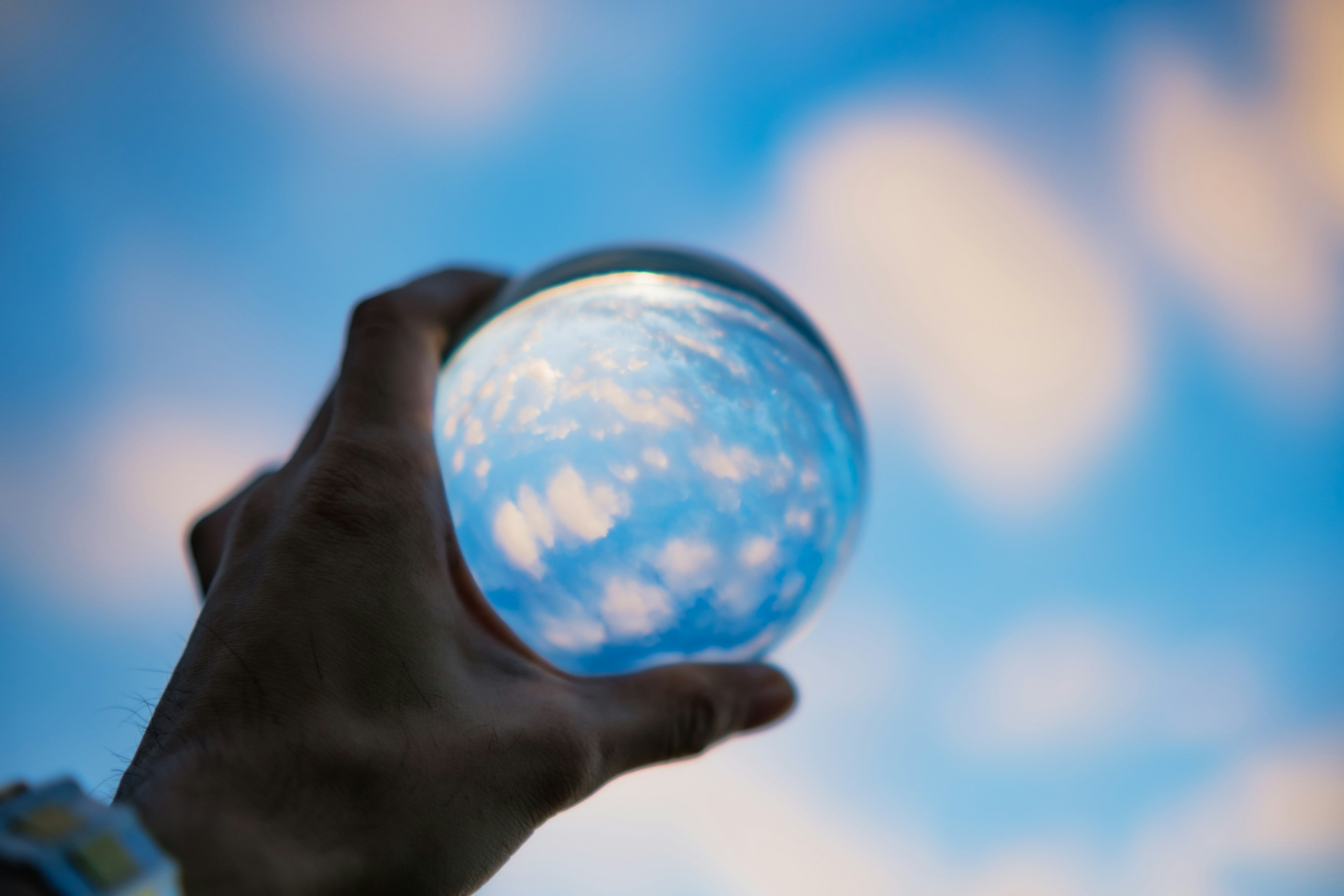 Una sfera di cristallo tenuta in mano che riflette il cielo blu e le nuvole