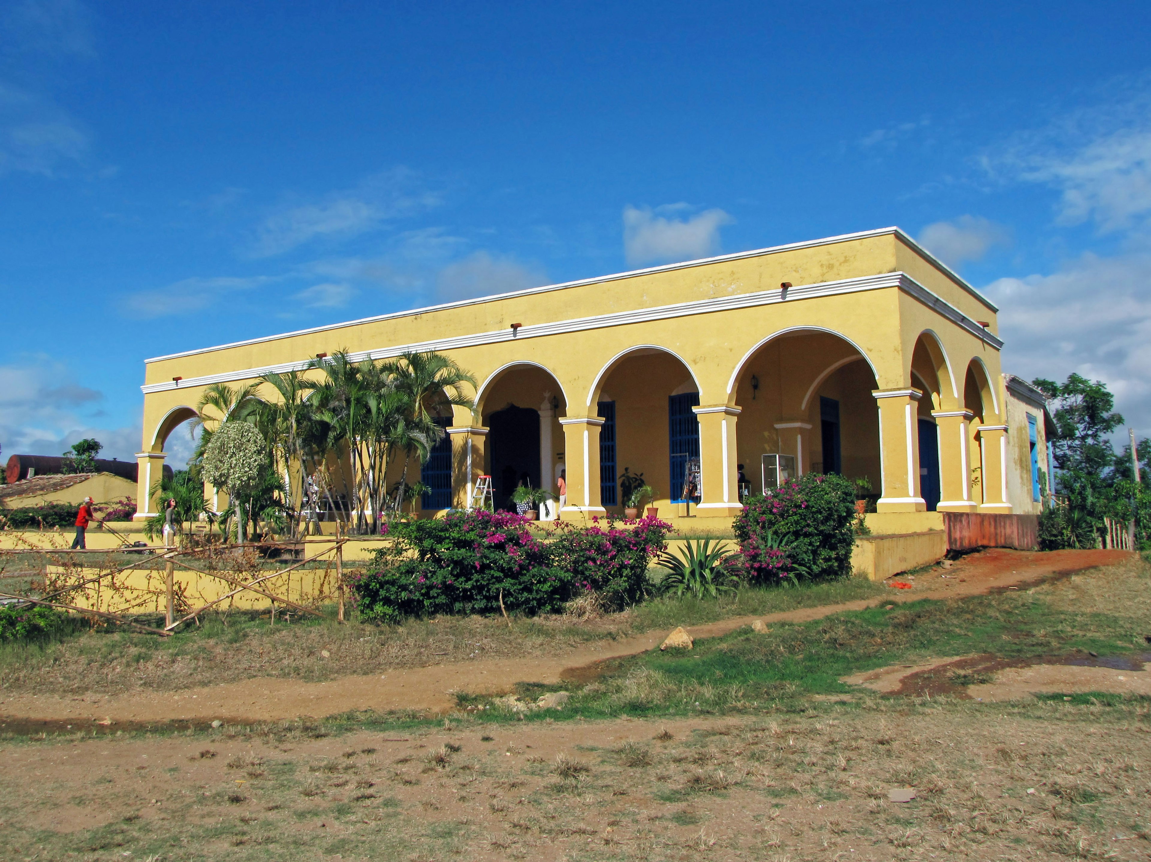 Yellow building with archways surrounded by greenery and blue sky