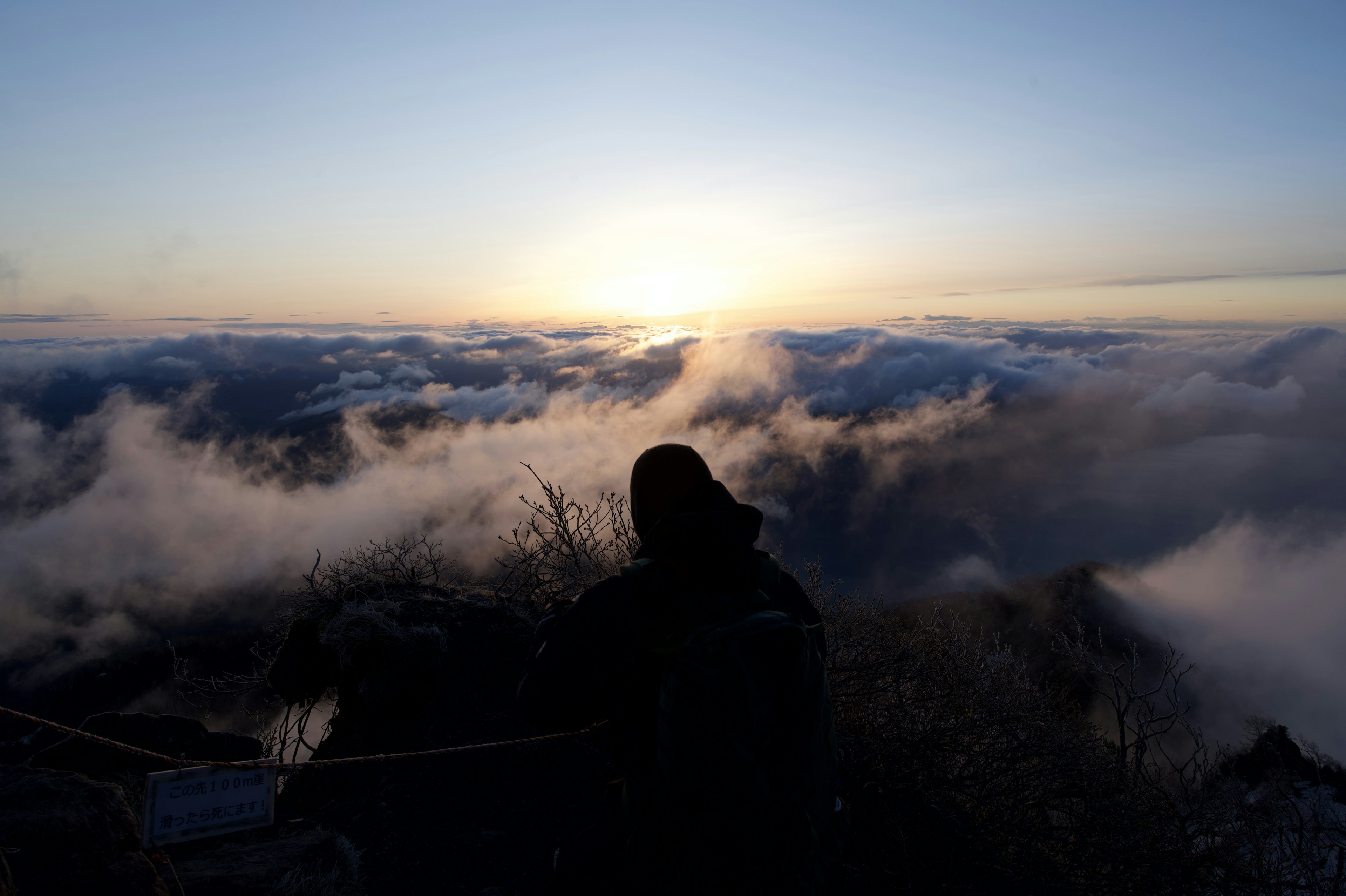 山頂からの朝焼けを見つめる人物と雲海の景色