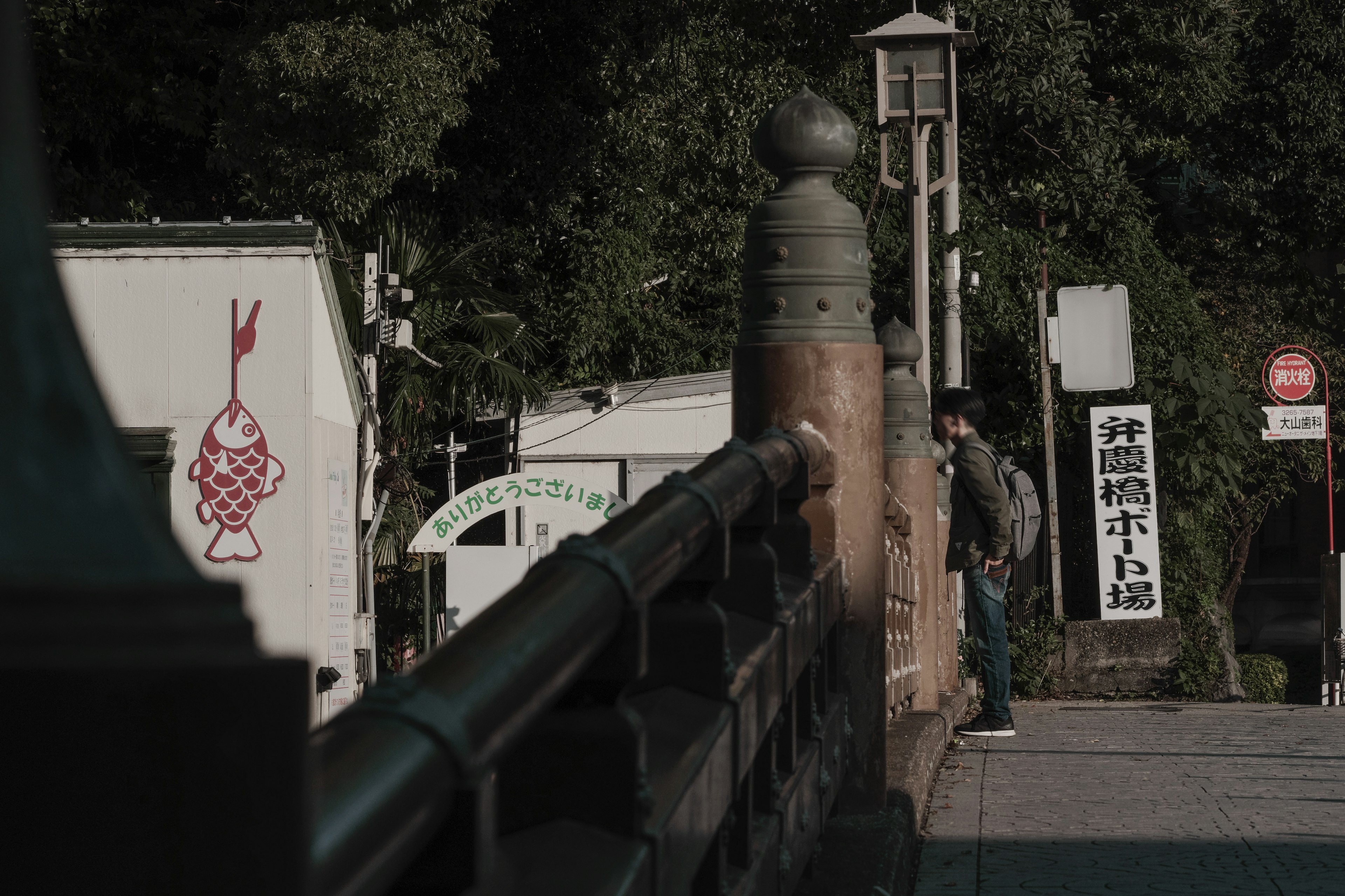 A person standing near a bridge with a visible sign in the background