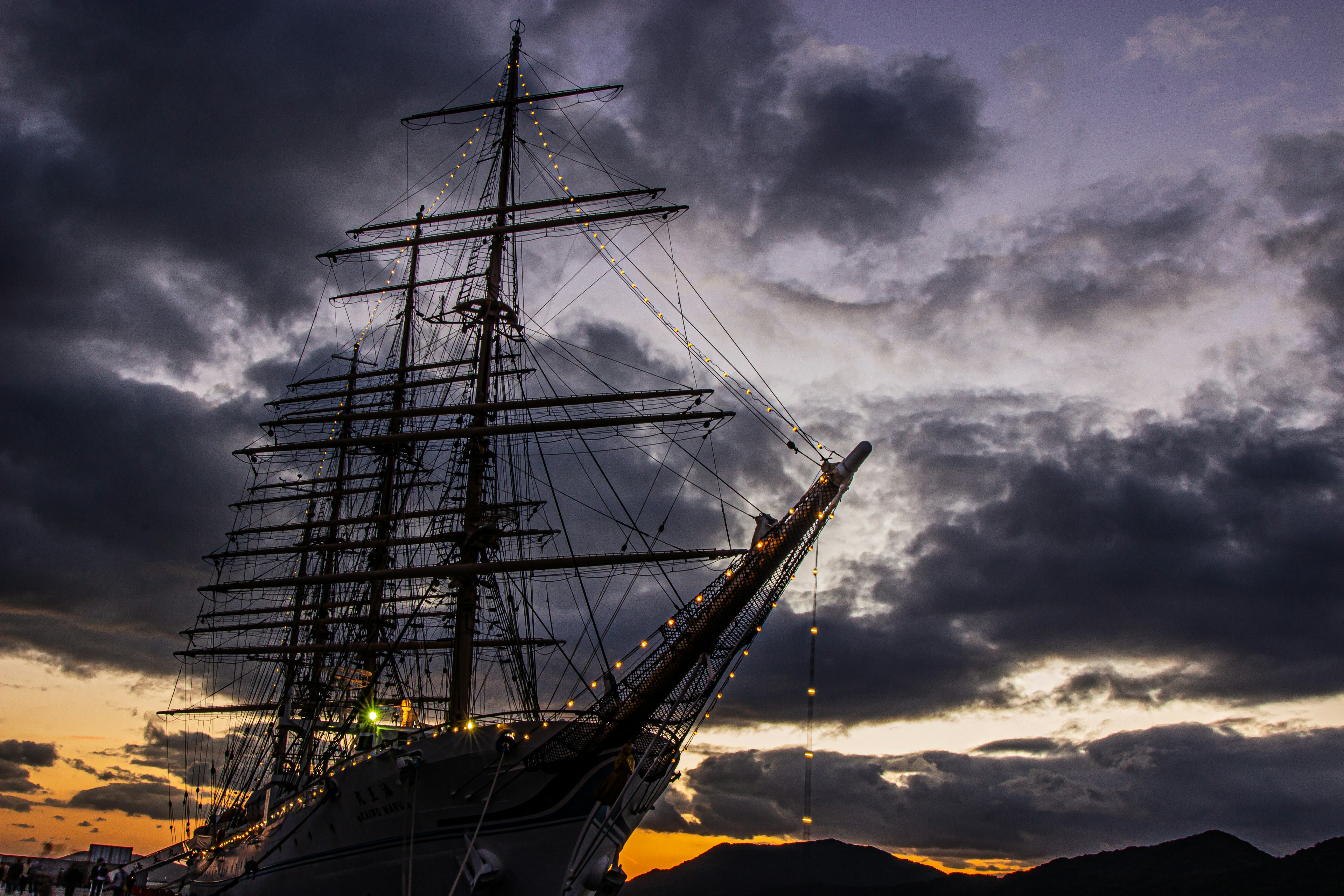 Silhouette of a large sailing ship against a sunset sky with dramatic clouds