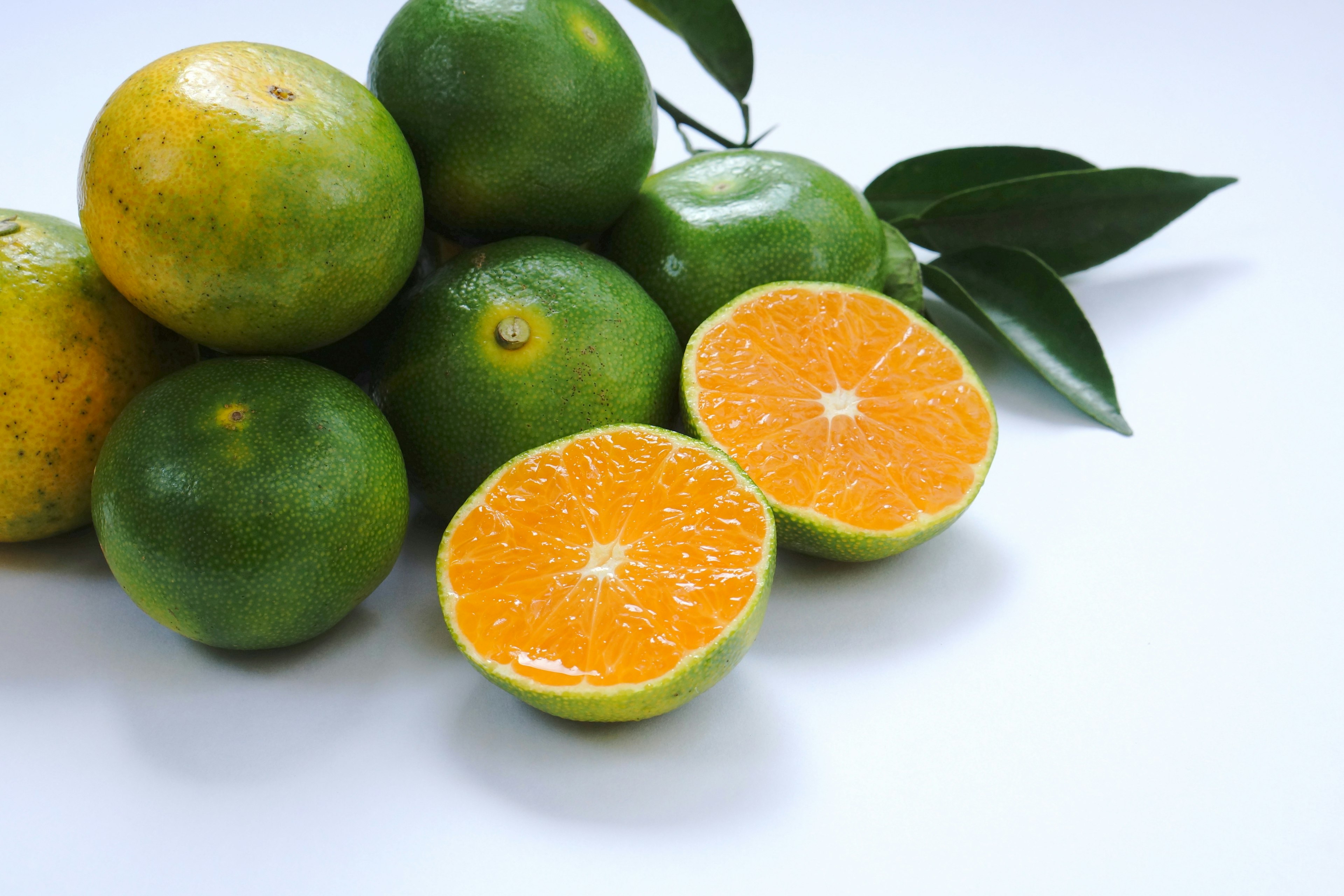 A cluster of green oranges with a halved orange showcasing its bright flesh