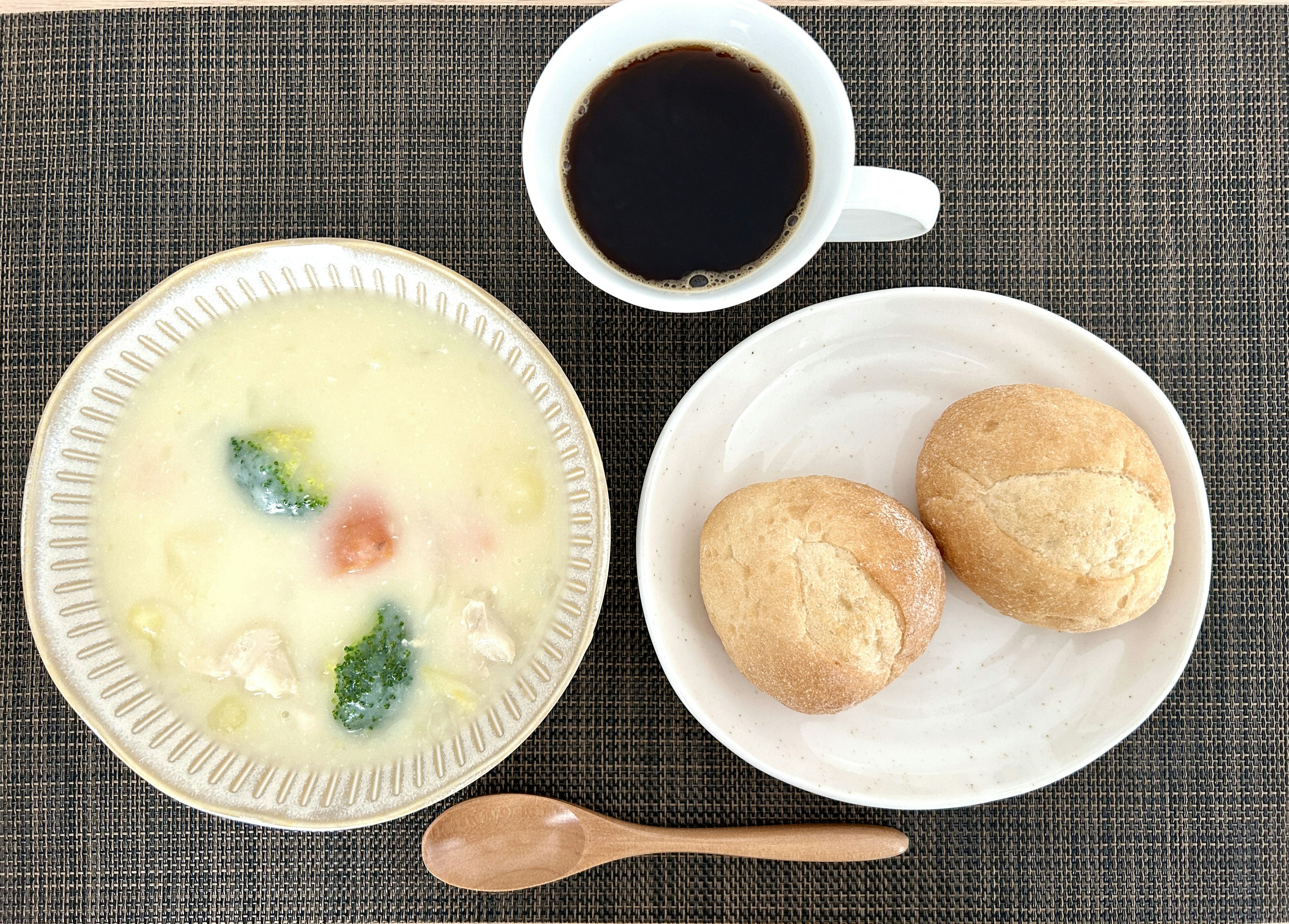 Mesa de desayuno con un tazón de sopa y dos bollos junto a una taza de café