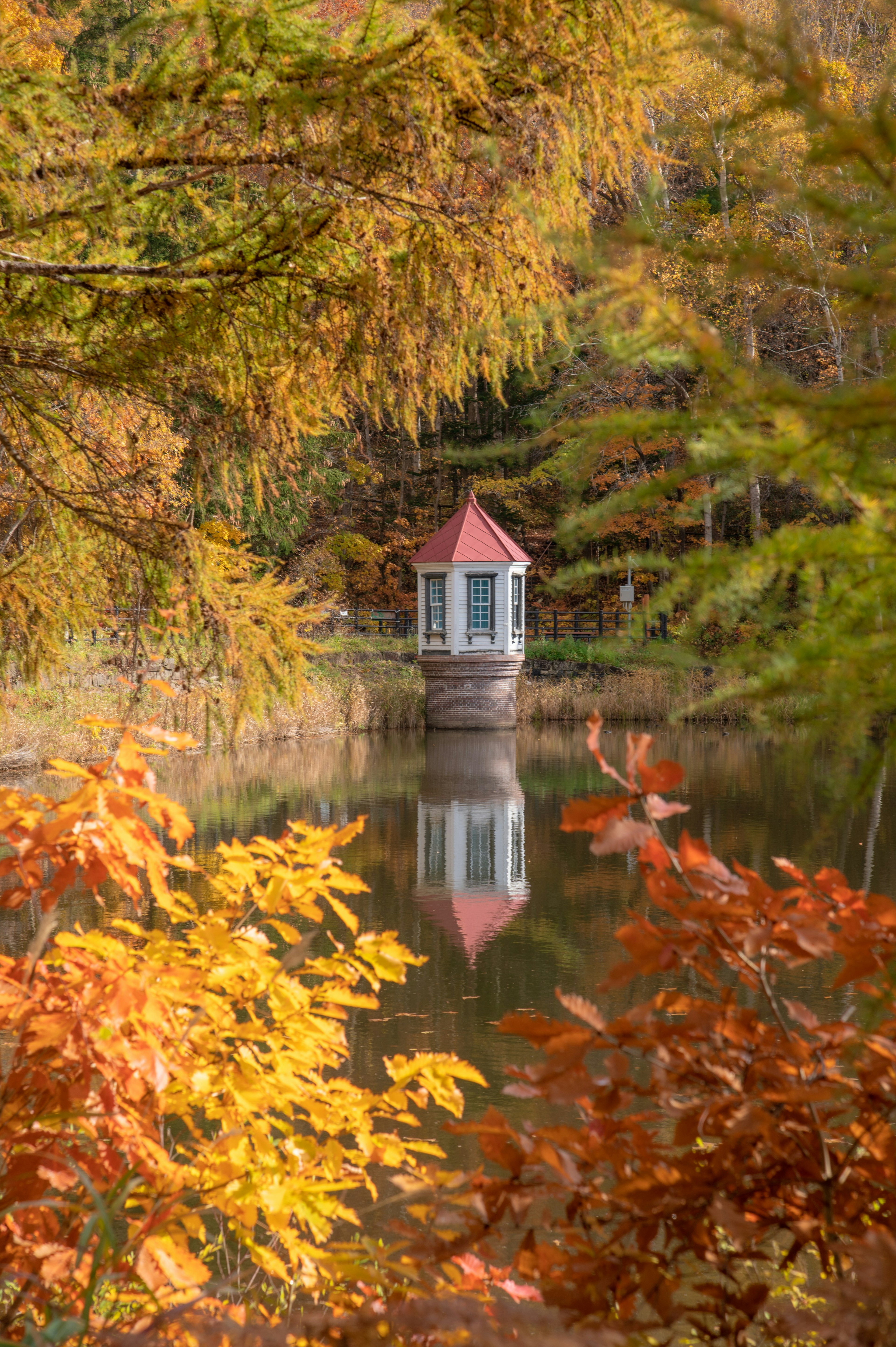 A small gazebo surrounded by autumn foliage reflected on a serene lake