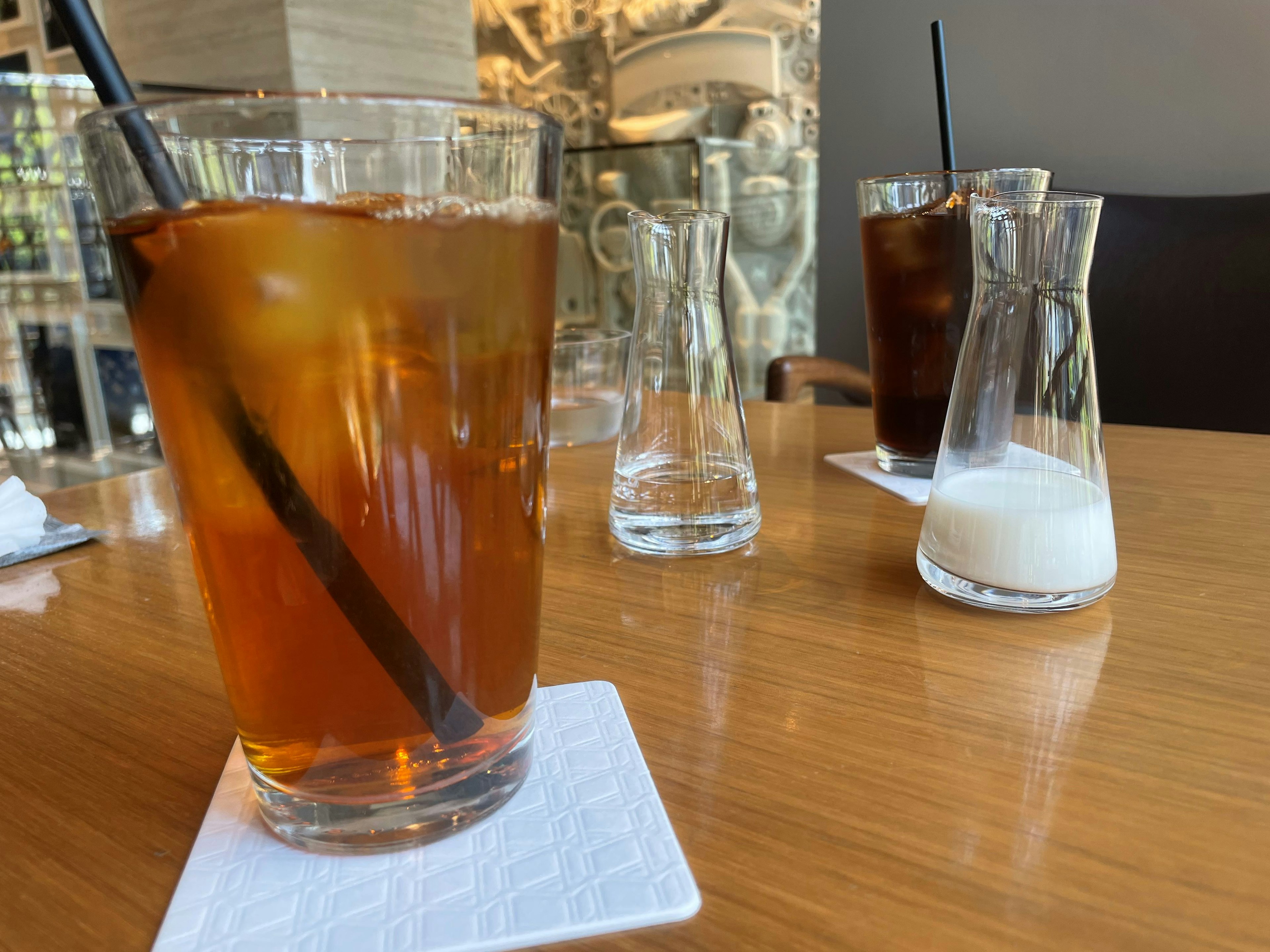 A glass of iced tea and coffee on a wooden table with cream and water