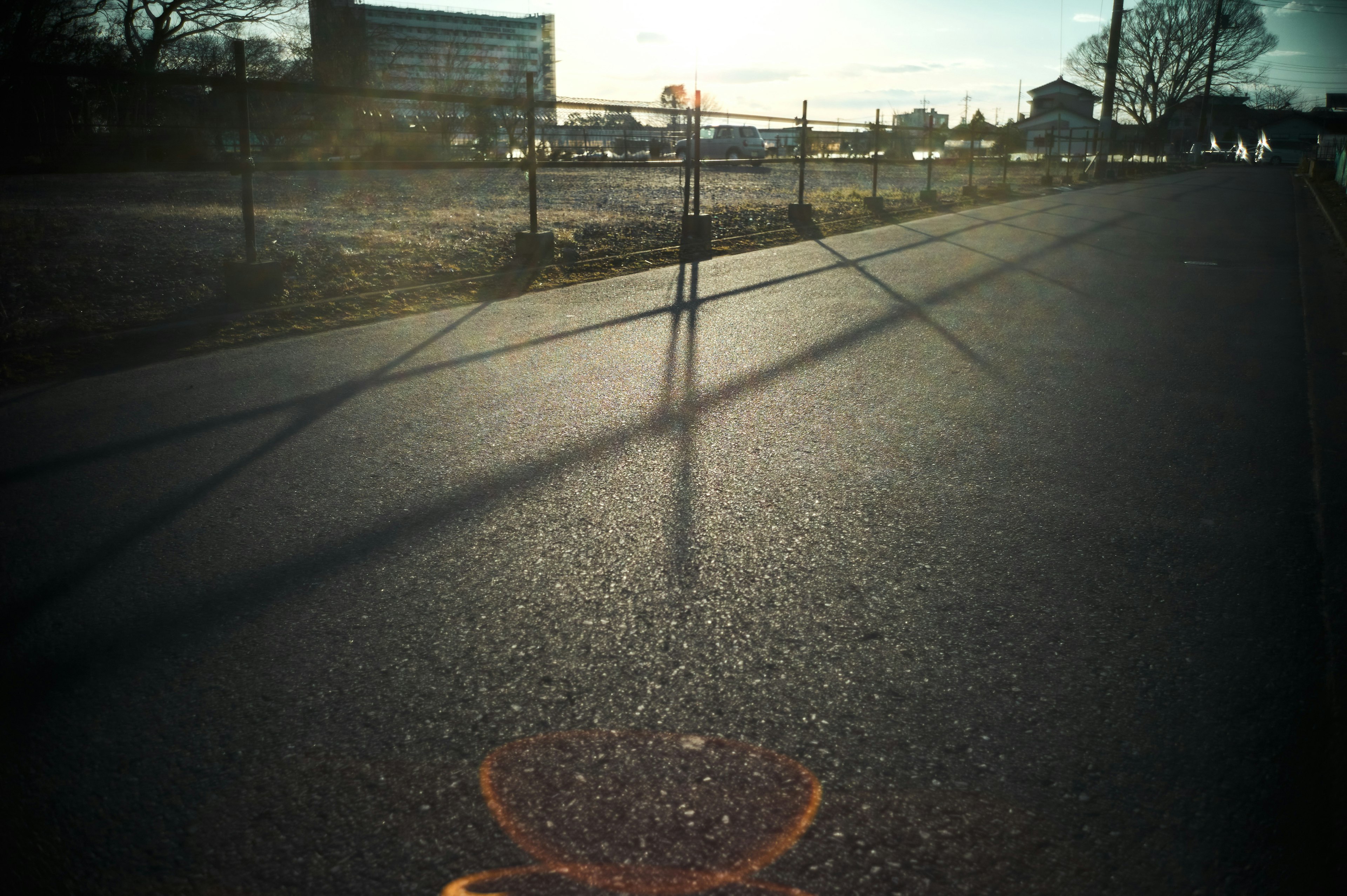 Una escena de una carretera pavimentada con largas sombras y edificios distantes