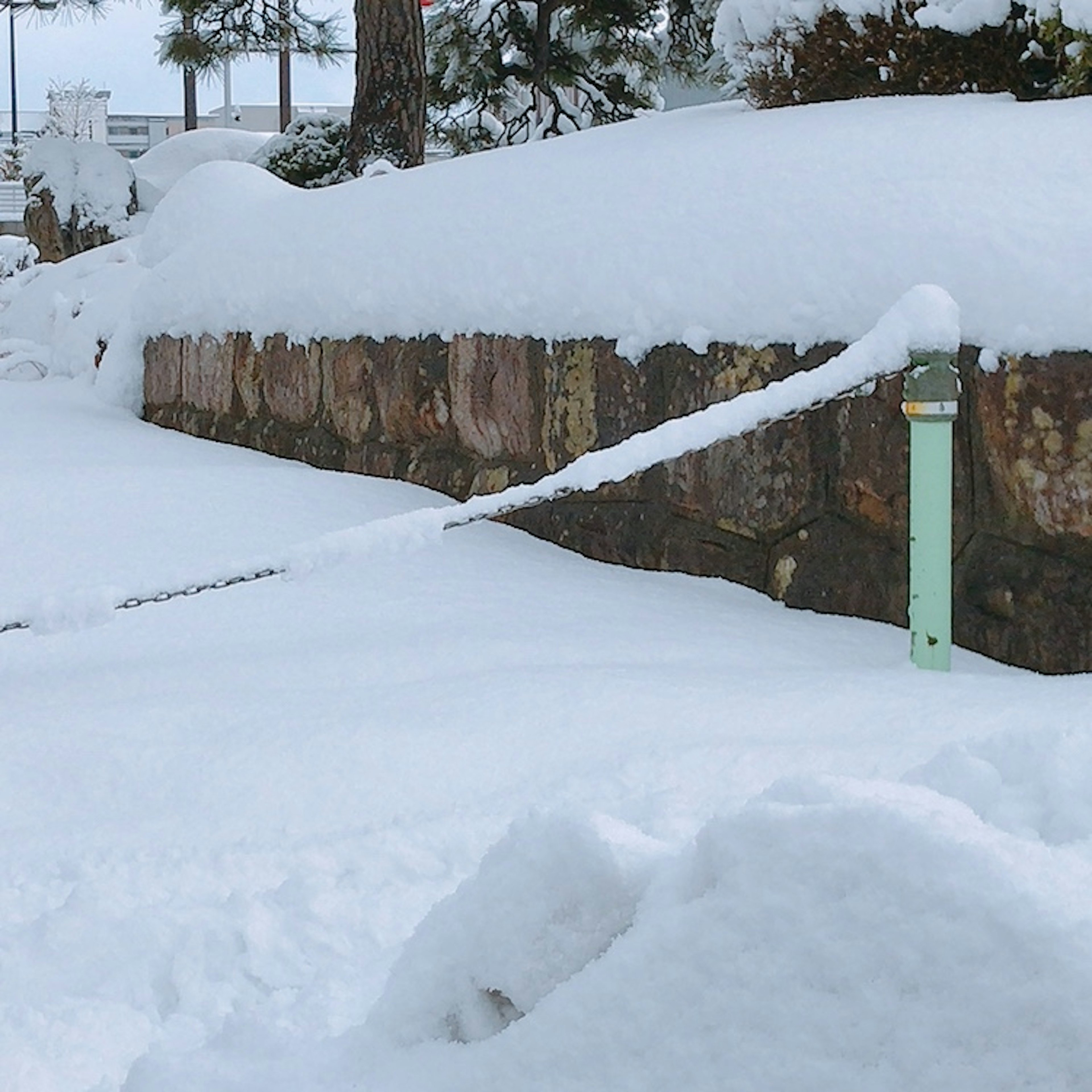 Schneebedeckte Landschaft mit einer Steinmauer und einem grünen Pfosten