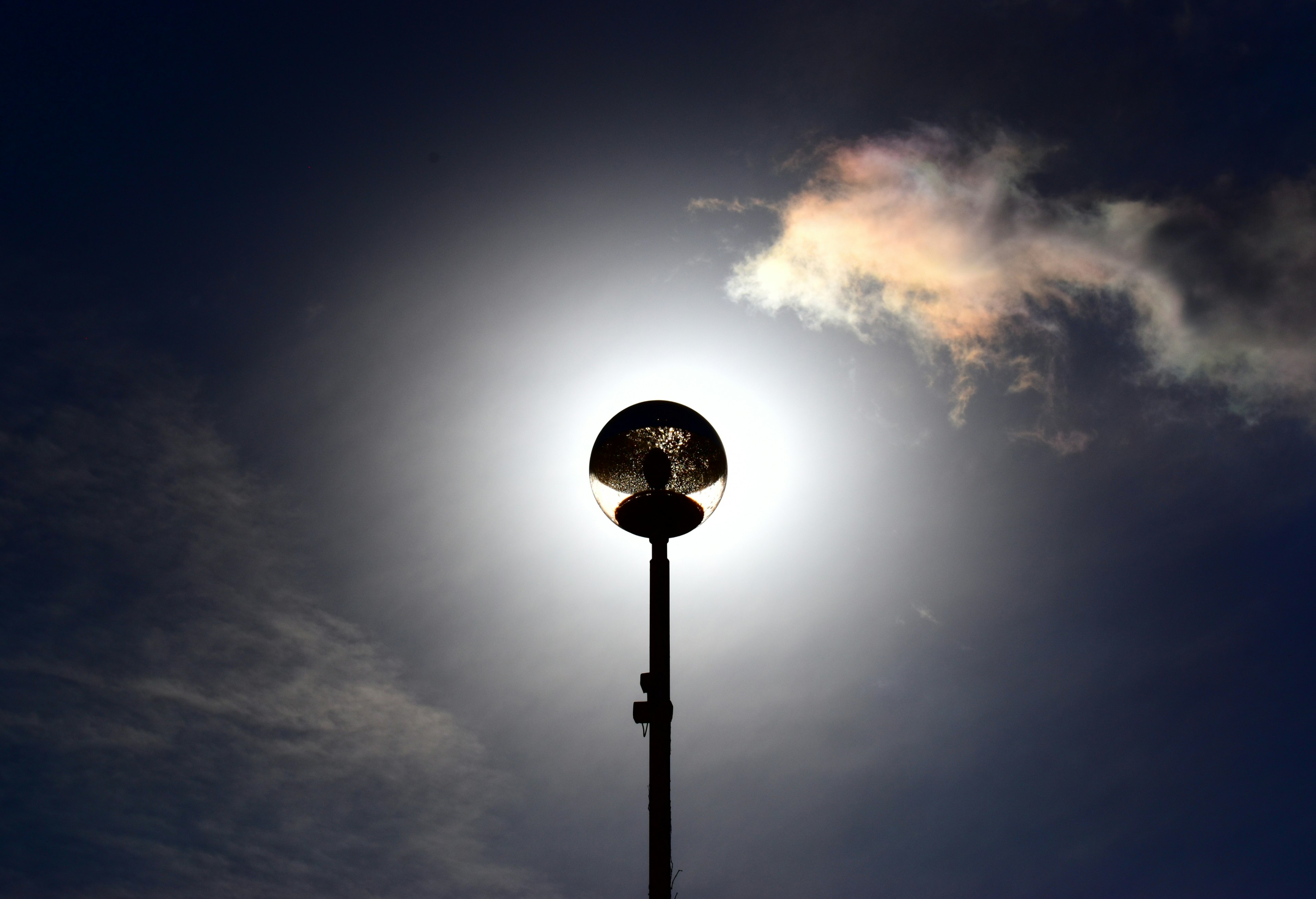 A streetlight silhouetted against a bright sky with clouds