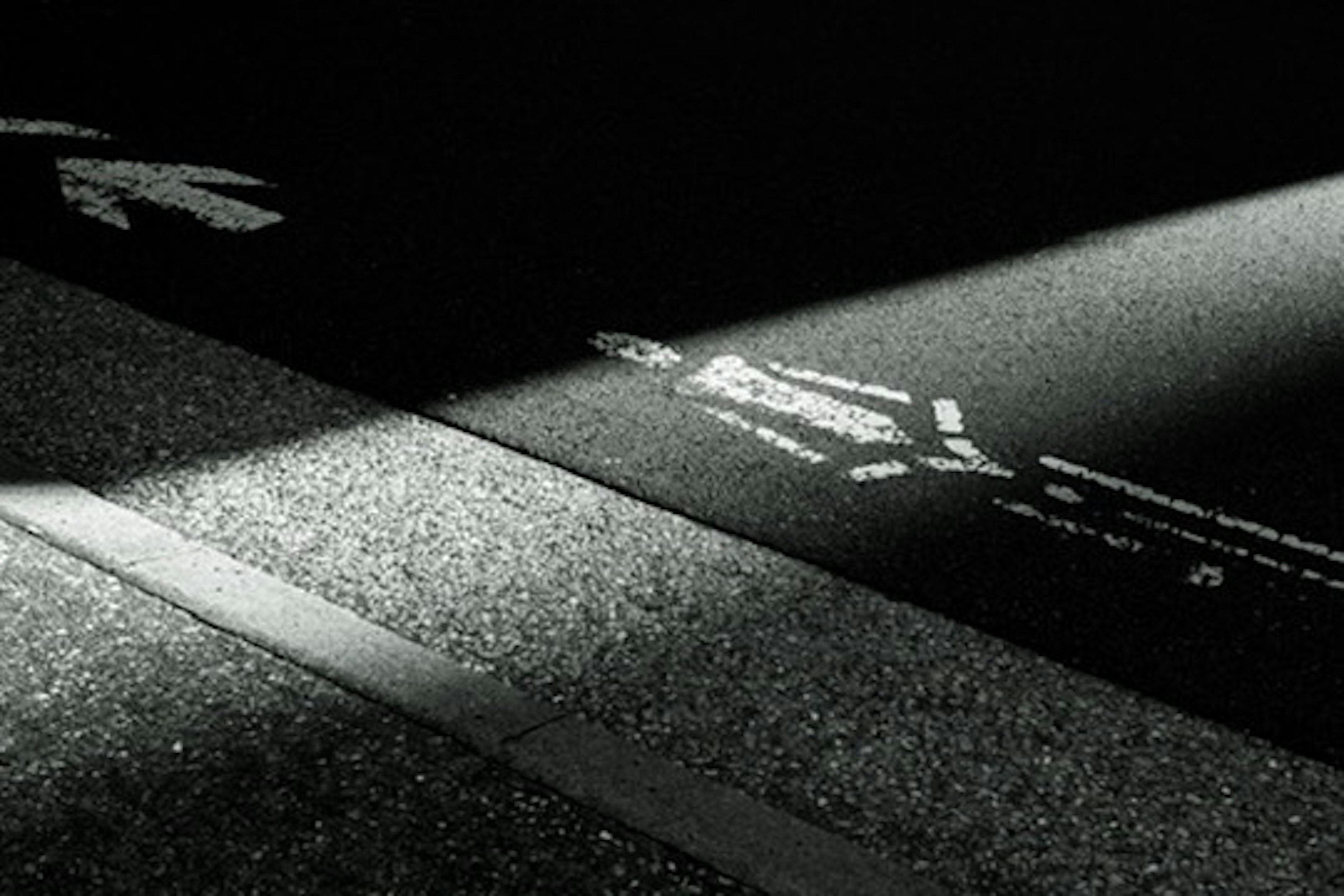 White pedestrian markings and arrows on a dark road illuminated by light