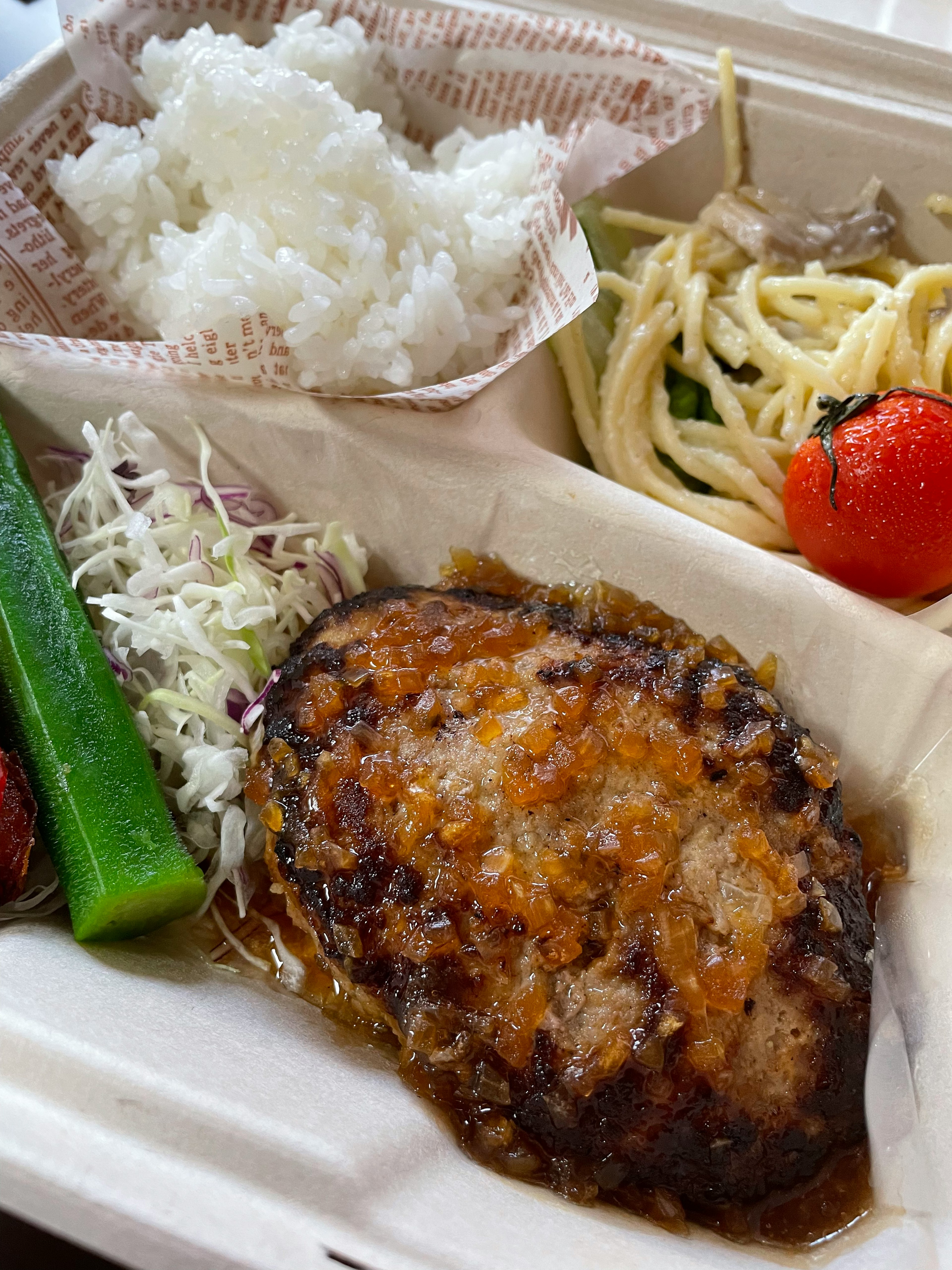 ご飯、ハンバーグ、サラダ、スパゲッティ、トマトを含む弁当