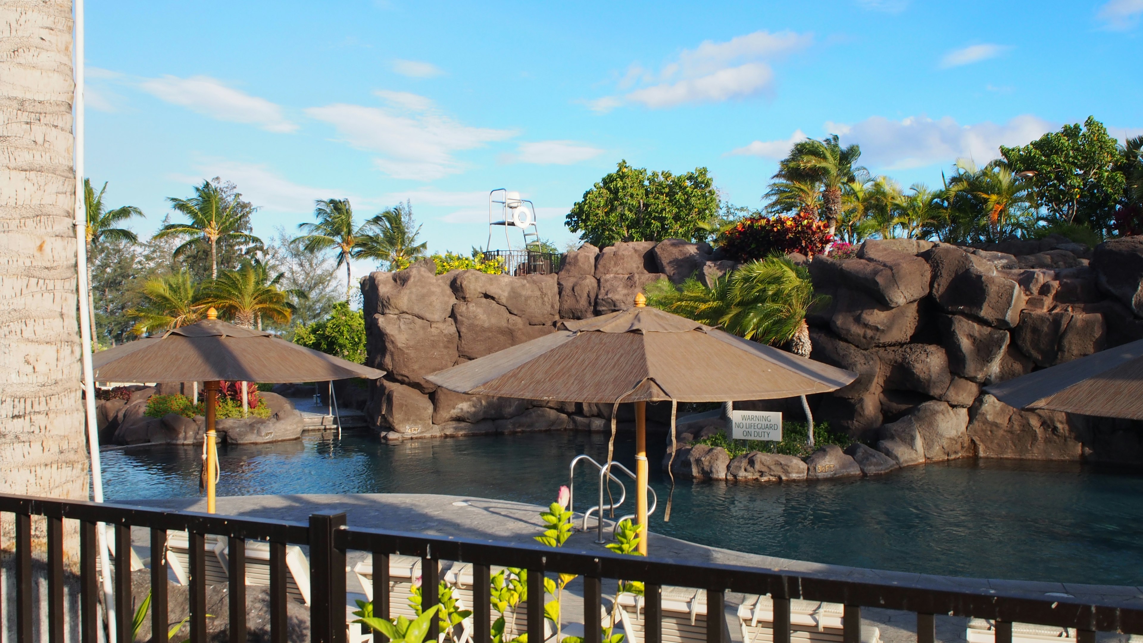 Resort pool area featuring a rocky backdrop and shaded umbrellas