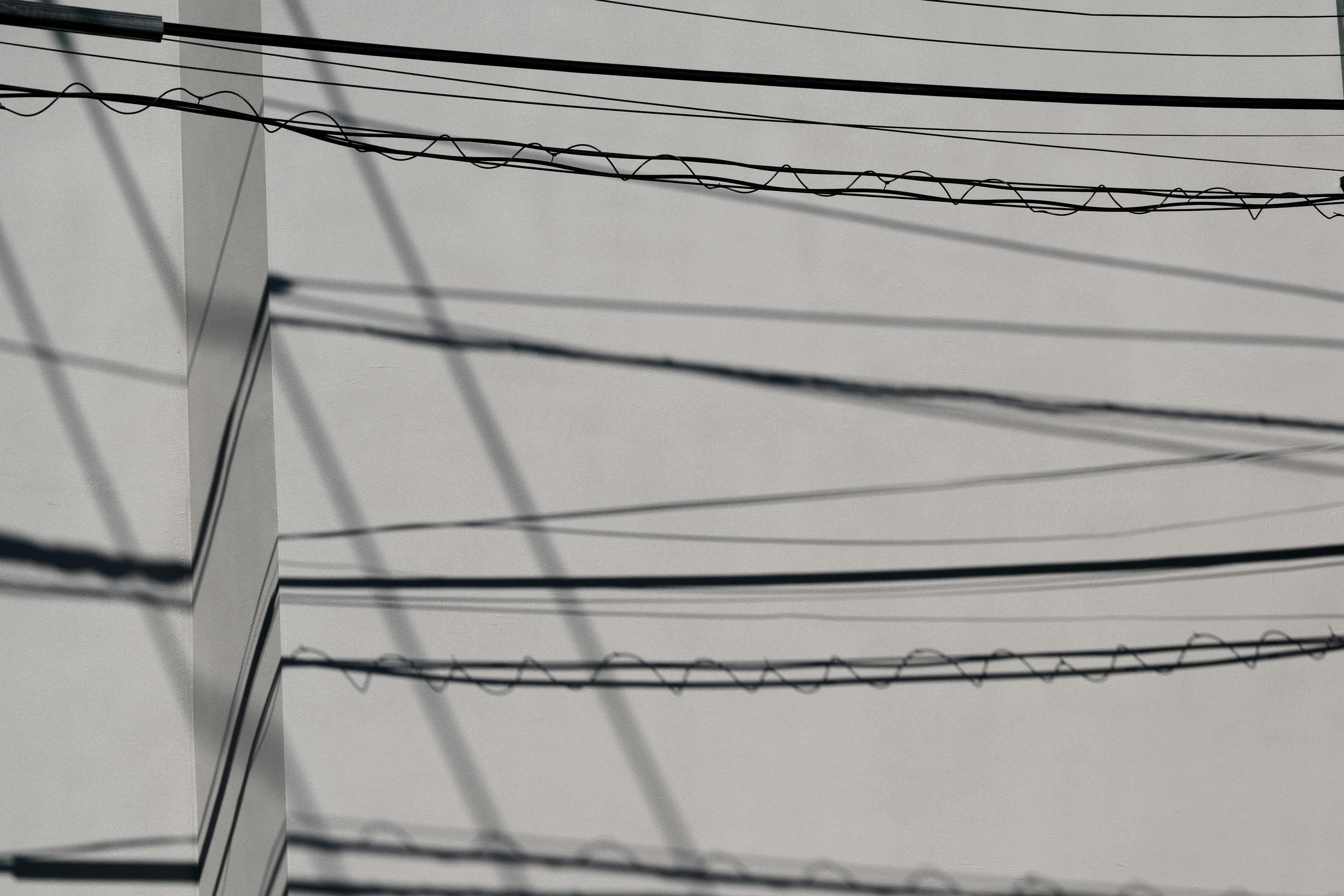 Una composizione semplice di ombre di linee elettriche che si incrociano su un muro bianco