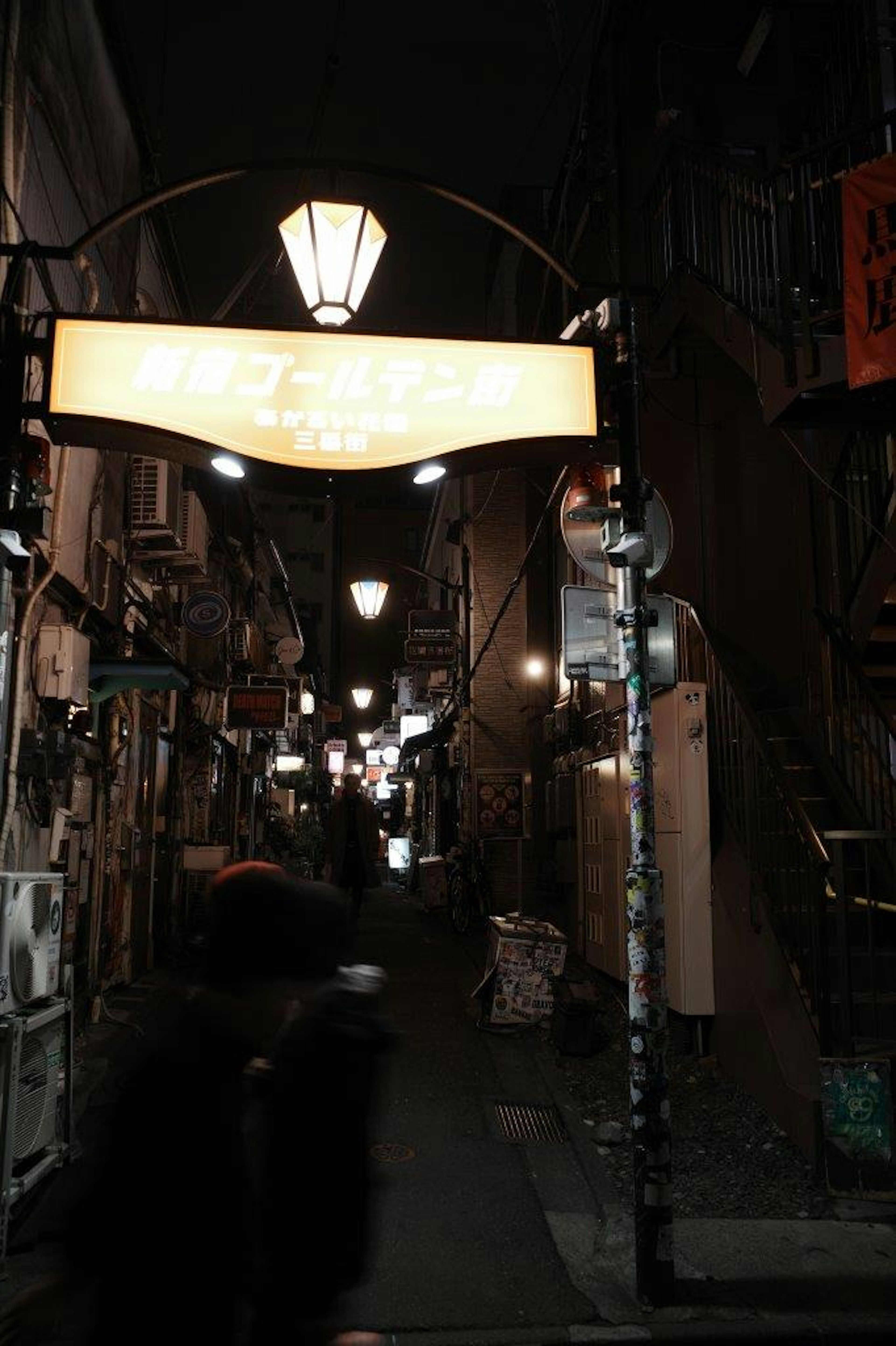 Callejón estrecho de noche con letrero iluminado y farolas vintage