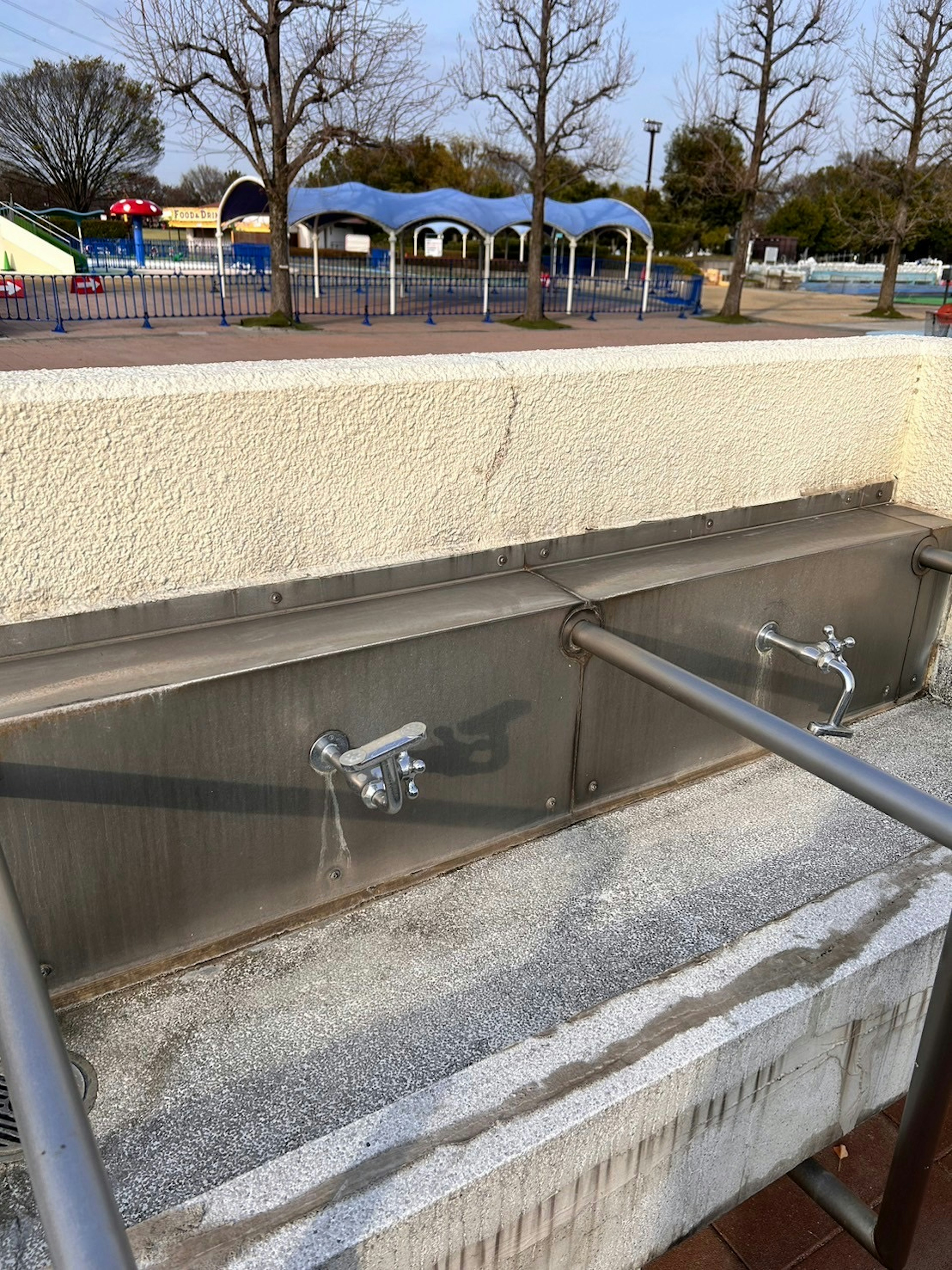 Metal sink and faucets in a park setting with trees in the background