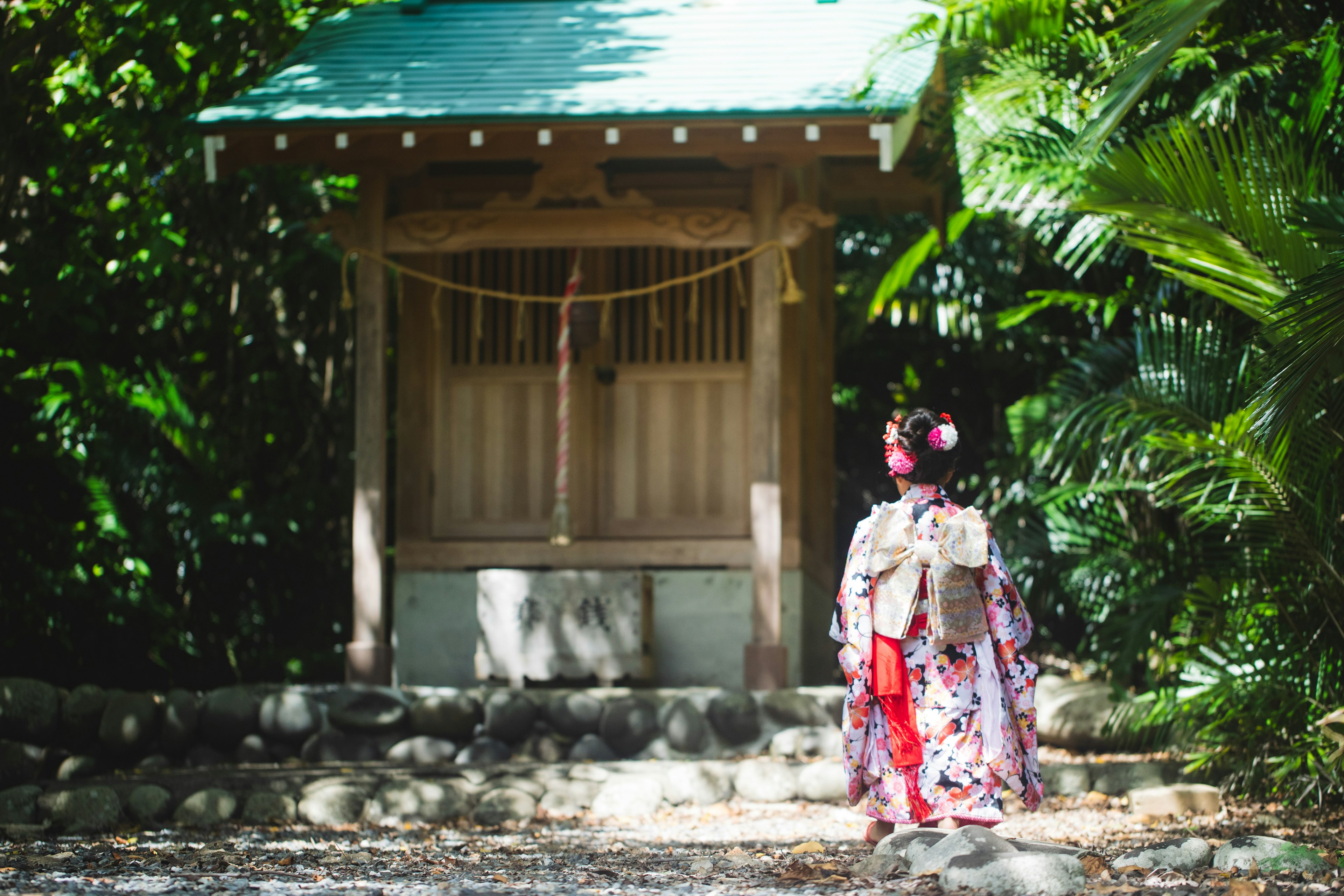 緑豊かな環境で伝統的な着物を着た女性が神社の前に立っています