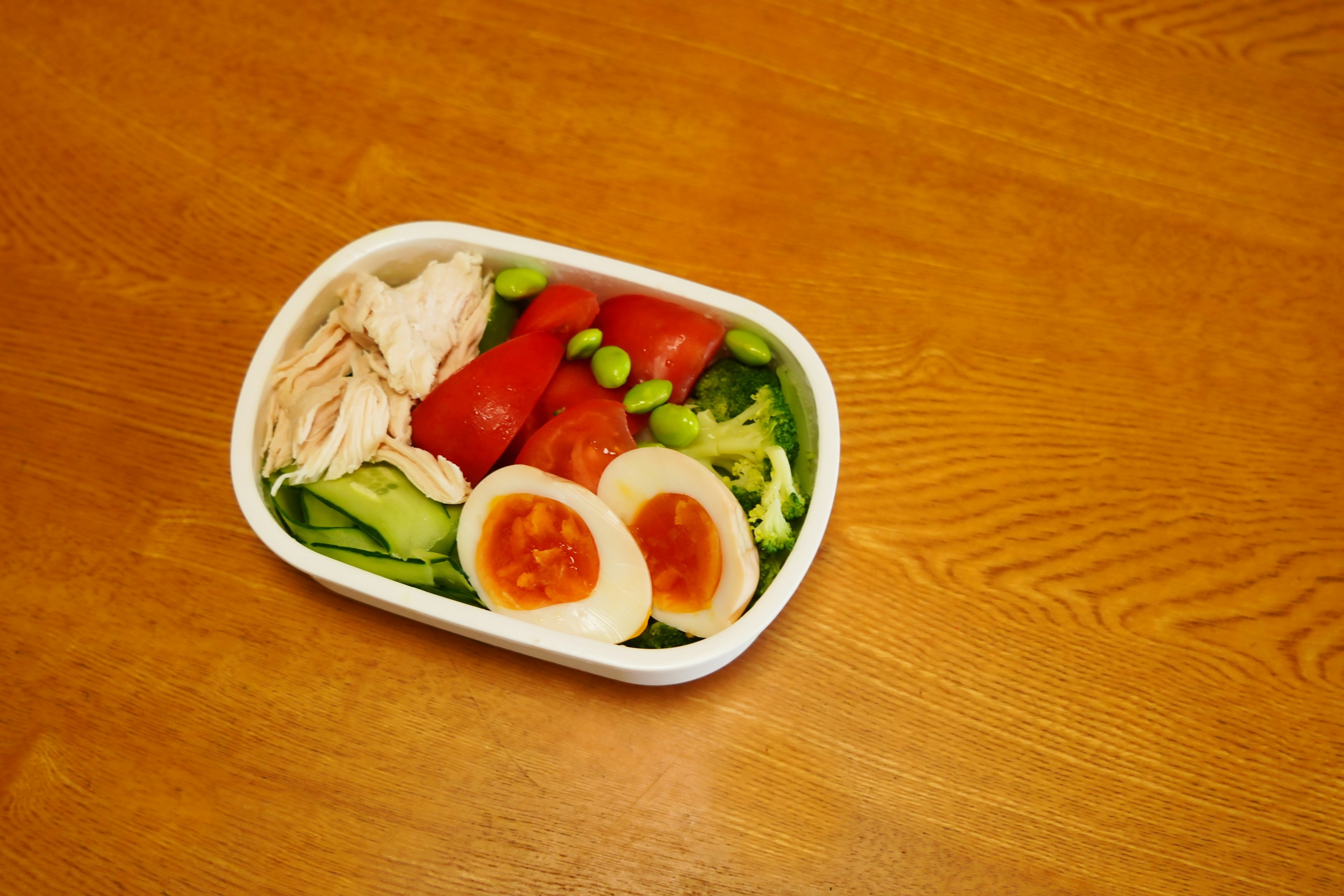 A white container filled with chicken, tomatoes, boiled eggs, and a salad of vegetables