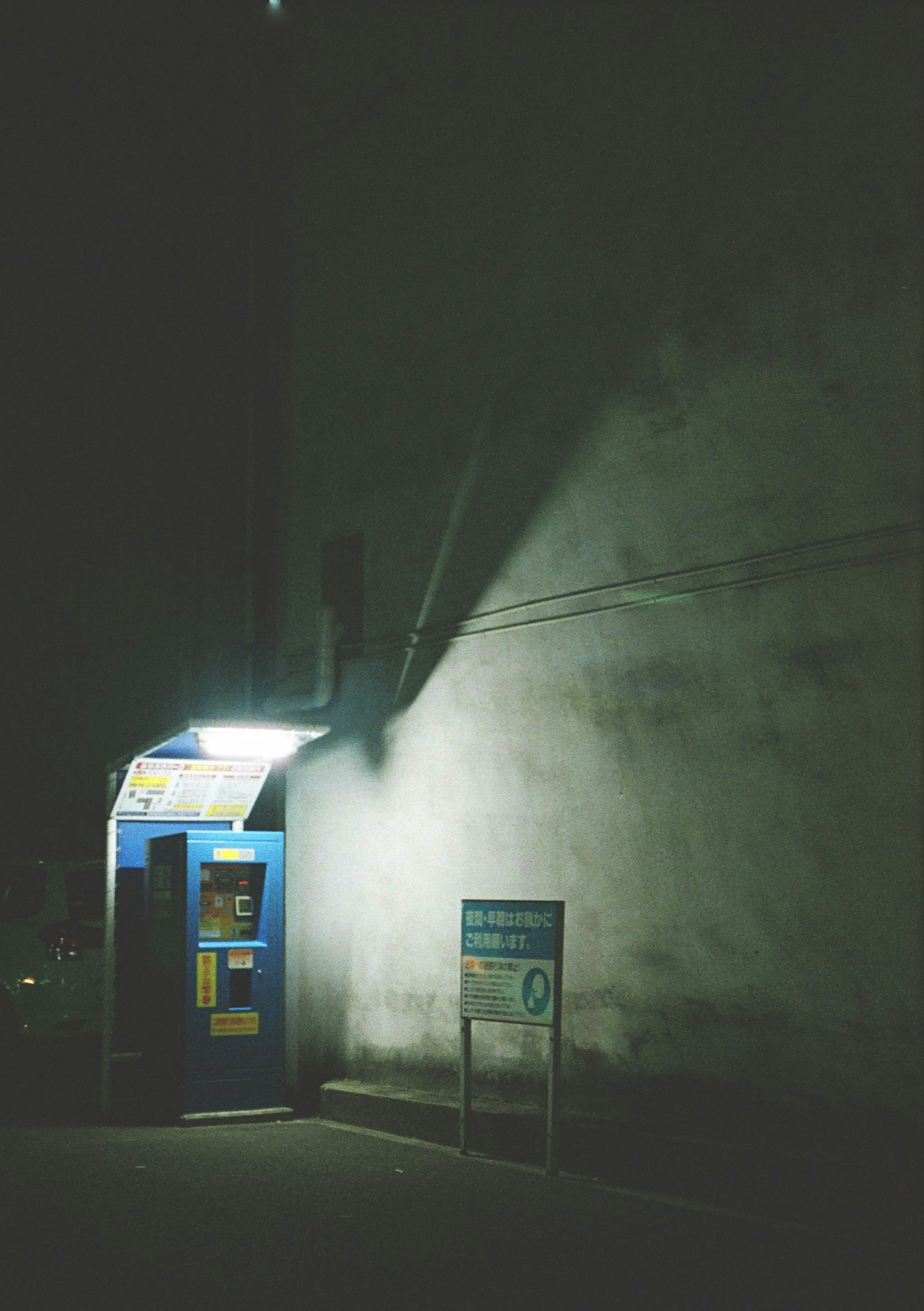 Cabina telefonica blu illuminata di notte con ombre sul muro