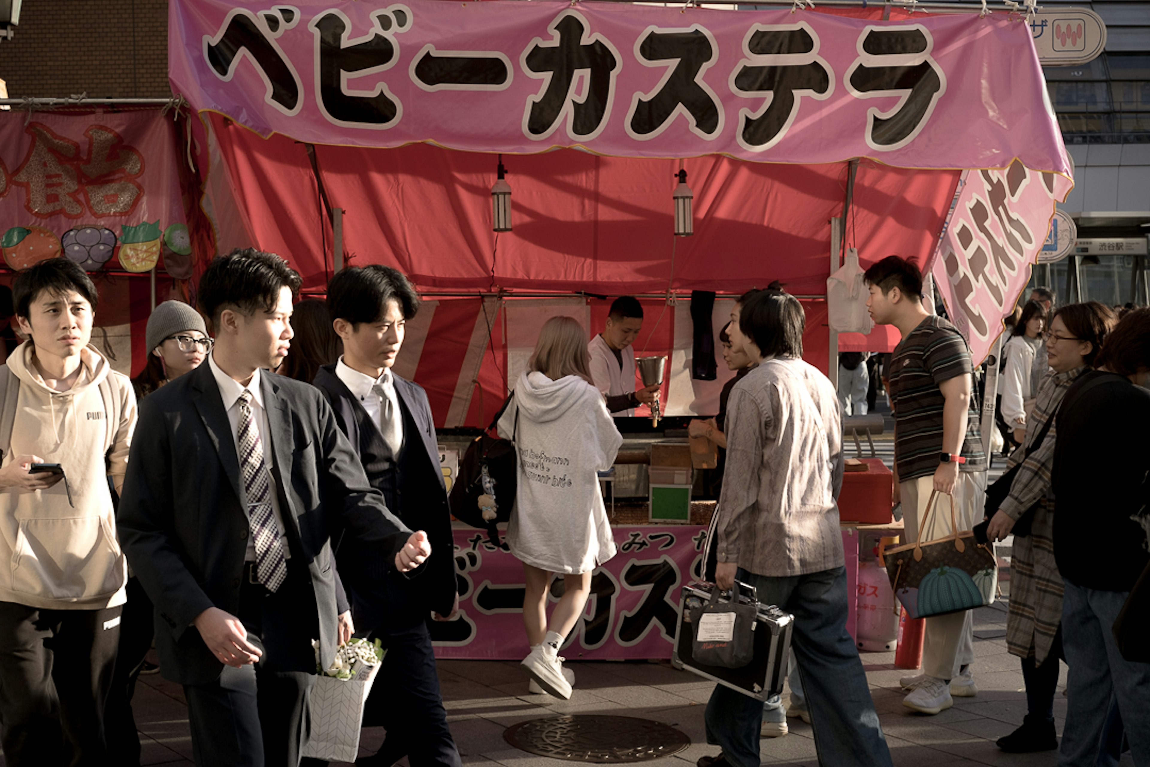 Busy street scene with people walking past a pink food stall