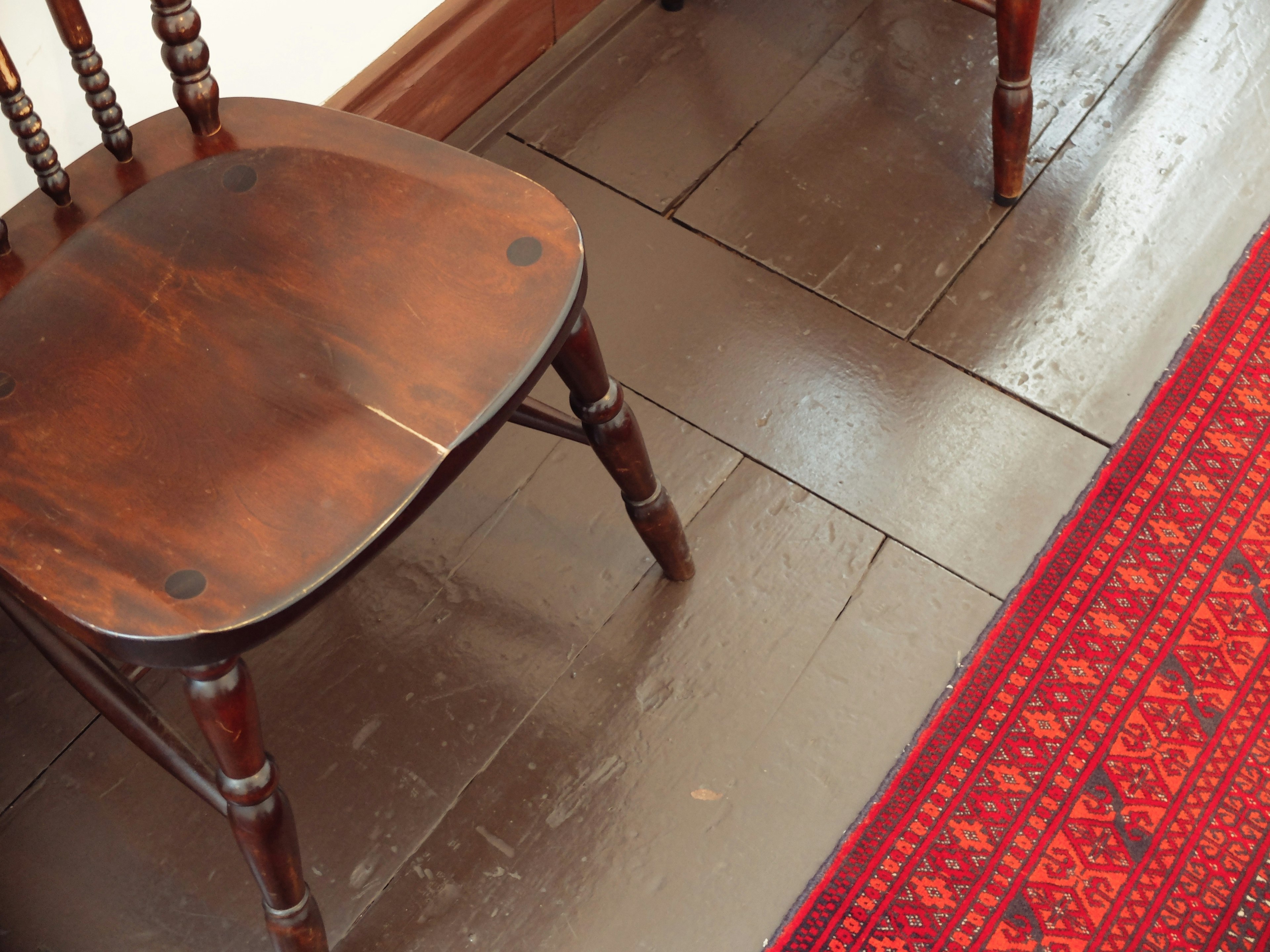 Una silla de madera junto a una alfombra roja con patrón en el suelo